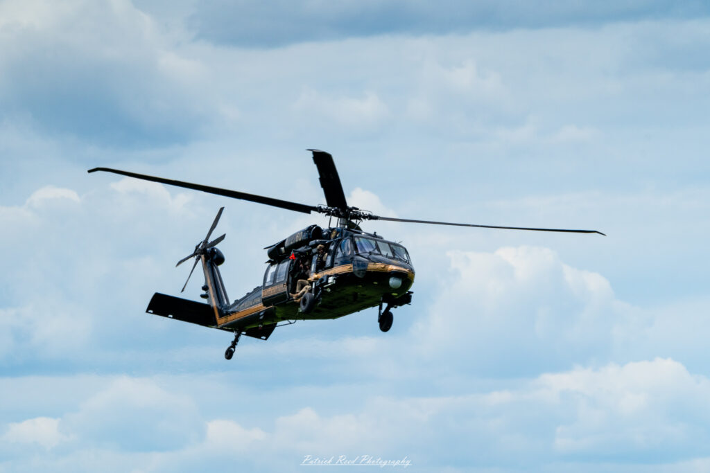 "A Black Hawk helicopter, in mid-flight, displaying its rugged and versatile design. The helicopter features a sleek, black exterior with a distinctive angular profile and large, powerful rotors that are in motion. Its robust frame and military insignia, such as the U.S. Army logo, are clearly visible. The Black Hawk is equipped for various roles including troop transport, medical evacuation, and reconnaissance. The backdrop of the scene may include a clear sky or a dramatic landscape, emphasizing the helicopter's capability and agility in both tactical and operational scenarios."