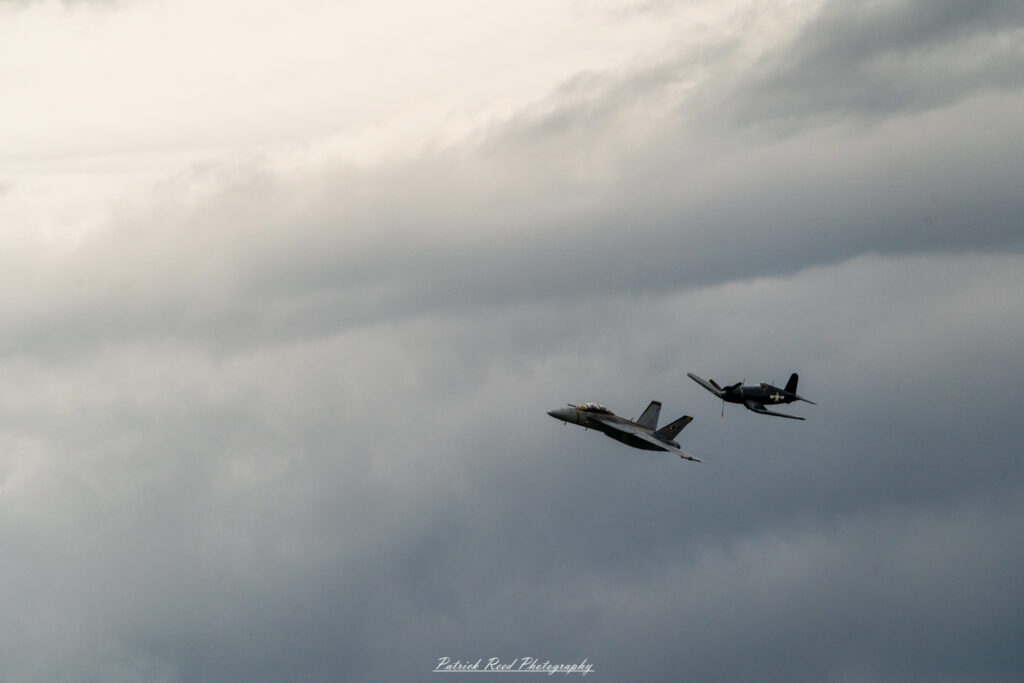 "An F-16 Fighting Falcon flying in formation alongside a P-51D Mustang, showcasing a striking contrast between two iconic fighter aircraft from different eras. The F-16, with its sleek, modern design, sharp lines, and powerful jet engine, flies smoothly next to the P-51D, which features a classic propeller-driven design with a bubble canopy and distinct WWII-era markings. The juxtaposition of the advanced, supersonic capabilities of the F-16 against the historic, rugged elegance of the P-51D highlights the evolution of military aviation and the enduring legacy of these legendary aircraft."