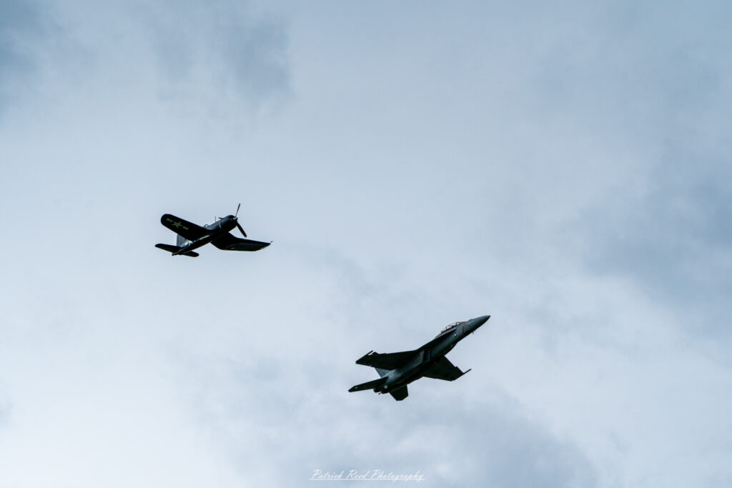 "An F-16 Fighting Falcon flying in formation alongside a P-51D Mustang, showcasing a striking contrast between two iconic fighter aircraft from different eras. The F-16, with its sleek, modern design, sharp lines, and powerful jet engine, flies smoothly next to the P-51D, which features a classic propeller-driven design with a bubble canopy and distinct WWII-era markings. The juxtaposition of the advanced, supersonic capabilities of the F-16 against the historic, rugged elegance of the P-51D highlights the evolution of military aviation and the enduring legacy of these legendary aircraft."