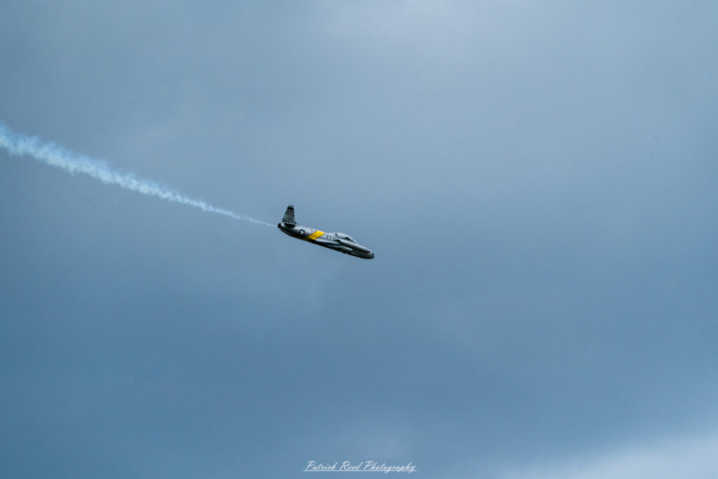 "The Lockheed T-33, a classic jet trainer aircraft, is depicted in a striking flight pose against a clear blue sky. This aircraft features a sleek, streamlined design with a distinct nose and a low-wing configuration. The T-33 is painted in a vibrant color scheme, often showcasing military markings and insignia. Its twin-engine layout and bubble canopy give it a distinctive appearance, emphasizing its role as an advanced trainer for pilots. The image captures the T-33's historical significance in aviation, highlighting its contribution to training generations of military aviators."