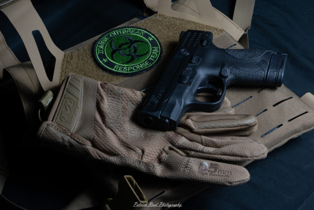 "A Smith & Wesson M&P Shield pistol leaning against a set of body armor. The scene emphasizes a sense of readiness and tactical preparedness, with the sleek, compact design of the handgun contrasting against the rugged, protective look of the body armor, symbolizing a balance between mobility and defense."