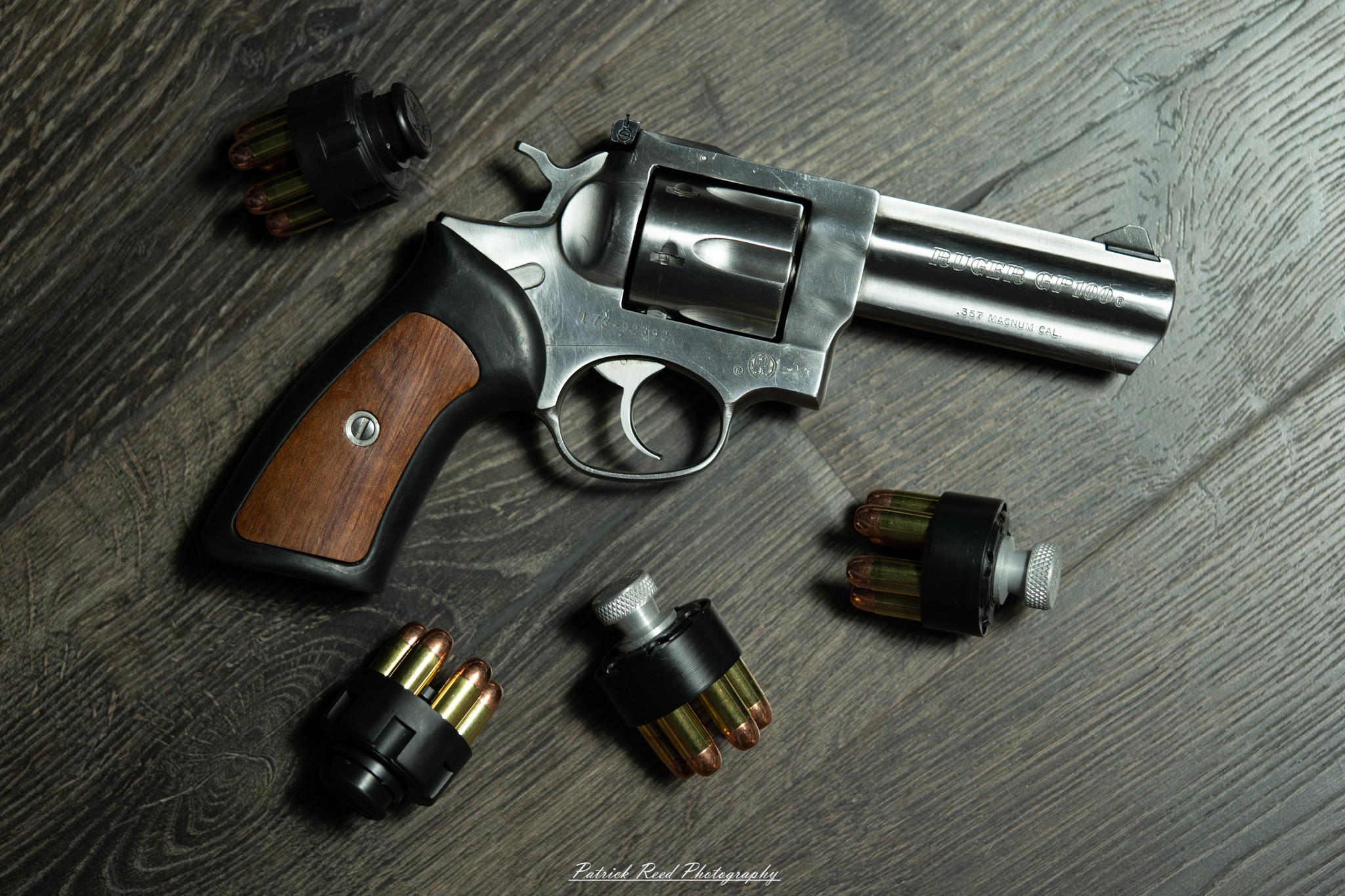 "A Ruger GP100 revolver displayed on a flat surface, with three speedloaders placed nearby. The scene emphasizes the robust build of the revolver, with its polished metal finish, alongside the speedloaders, highlighting the practicality and readiness for quick reloading in a classic, powerful firearm setup."