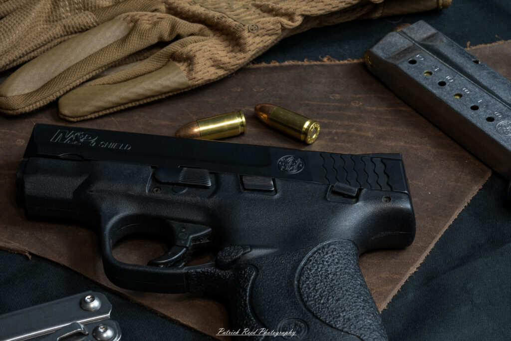 "A Smith & Wesson M&P Shield pistol placed on a piece of leather, with a magazine positioned beside it. The leather surface adds a touch of rustic sophistication, complementing the sleek, compact design of the firearm and its magazine, highlighting the blend of practicality and style."