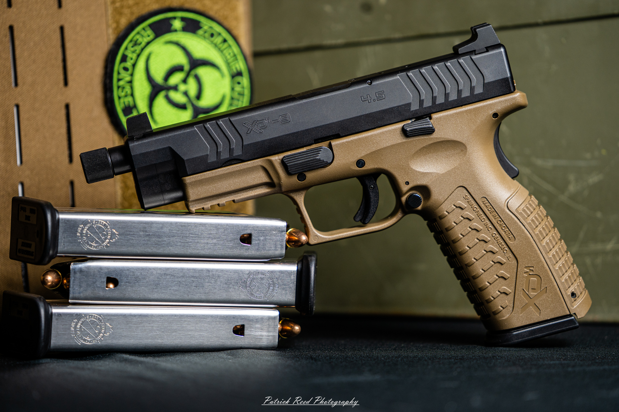 "A Springfield Armory XD-M pistol laid out on a flat surface, accompanied by three magazines positioned beside it. The arrangement showcases the pistol's design and the additional magazines, highlighting the practicality and readiness associated with this firearm."