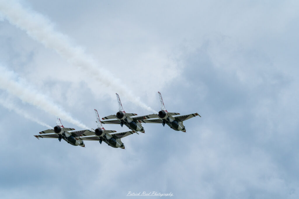 "The F-16 Thunderbirds, the U.S. Air Force's elite aerial demonstration team, flying in tight formation. These F-16 Fighting Falcons are painted in a striking red, white, and blue color scheme with bold, patriotic designs, including the iconic Thunderbird emblem on the tail. The jets perform precise, high-speed maneuvers, showcasing their agility and the pilots' exceptional skill. Trails of white smoke often follow the aircraft, adding to the dramatic visual display as they execute loops, rolls, and formations, symbolizing the power and precision of the U.S. Air Force."