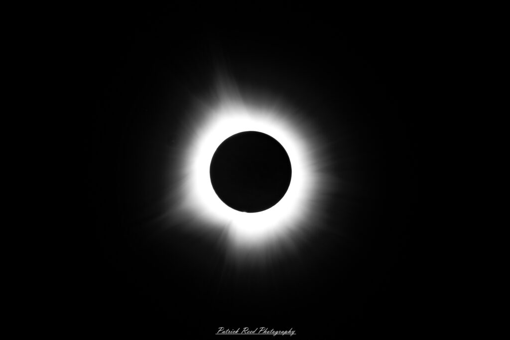 "Totality during a solar eclipse, the awe-inspiring moment when the moon completely covers the sun. In this dramatic phase, the sky darkens to a deep twilight, and the sun’s brilliant corona becomes visible, radiating a soft, ethereal glow around the black disk of the moon. The temperature drops, and a sense of eerie calm envelops the landscape. This rare and mesmerizing event captivates viewers, showcasing the full power and beauty of a total solar eclipse."