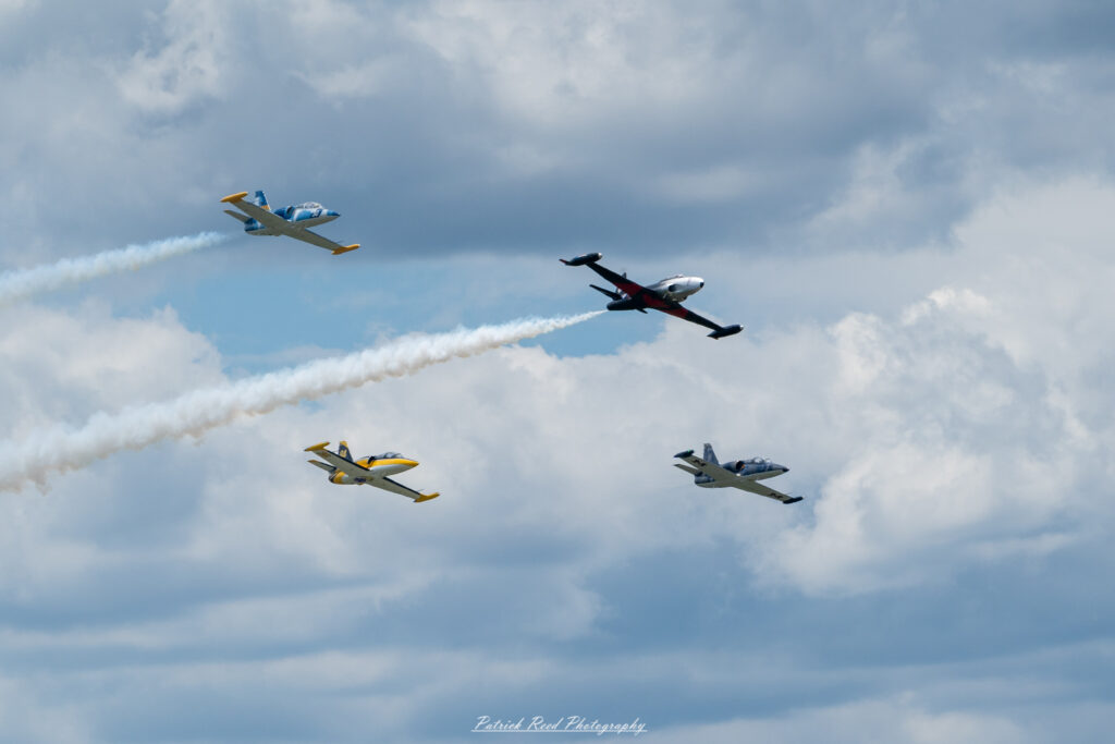 "Four vintage jets flying in tight formation against a clear blue sky, showcasing their classic designs and historical significance. Each aircraft, painted in vibrant colors and military markings from their respective eras, exhibits unique features, such as rounded noses, distinct tail designs, and sleek wings. The jets maintain precise spacing and altitude, creating a striking visual display that emphasizes teamwork and precision flying. This formation flight highlights the beauty and nostalgia of vintage military aviation, evoking memories of past conflicts and the evolution of aircraft technology."