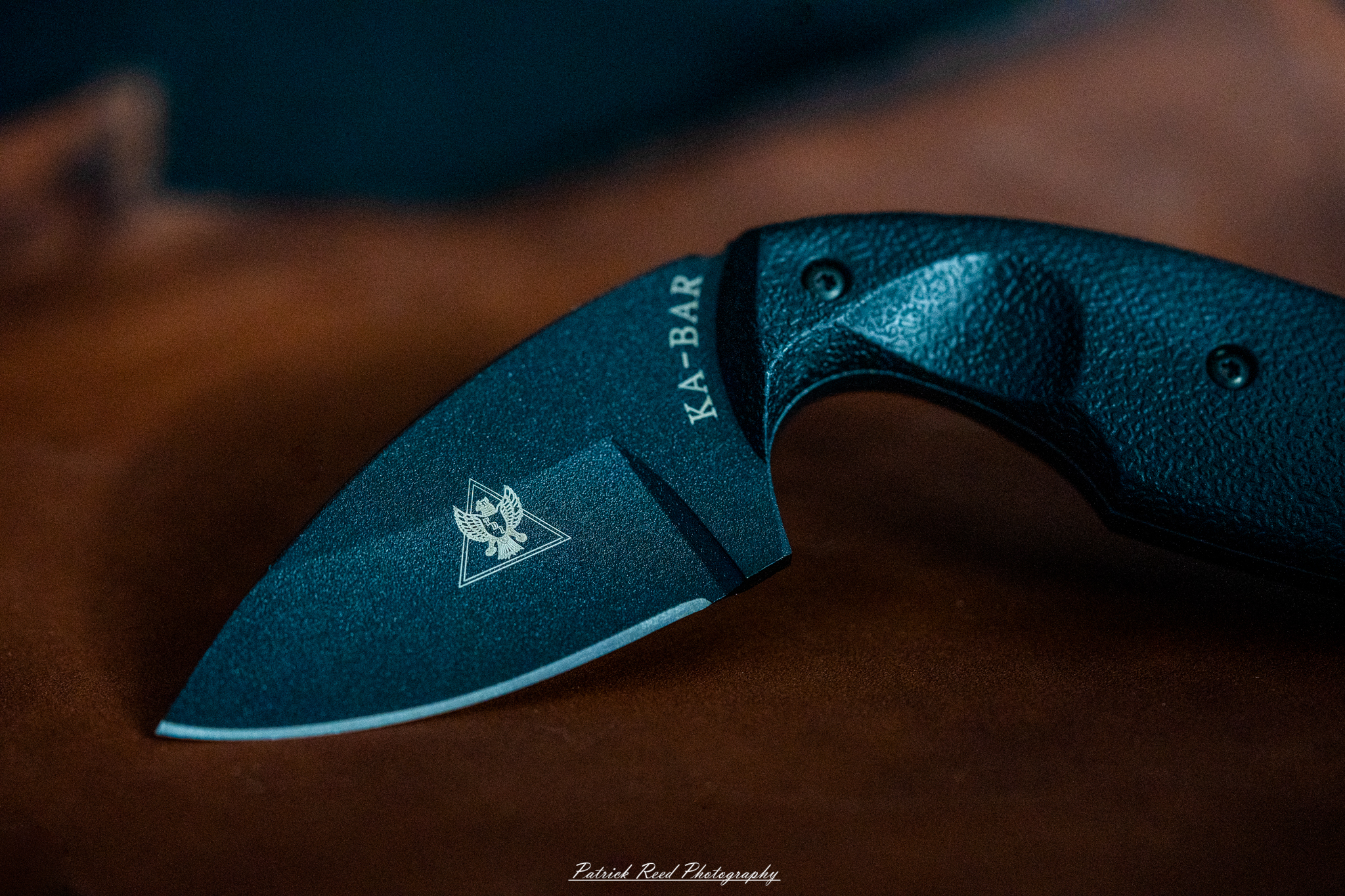 "A KA-BAR TDI knife resting on a piece of leather, showcasing its distinctive blade and ergonomic handle. The rich texture of the leather provides a rugged backdrop that highlights the knife's functionality and design, emphasizing its use as a practical tool for self-defense and everyday carry."