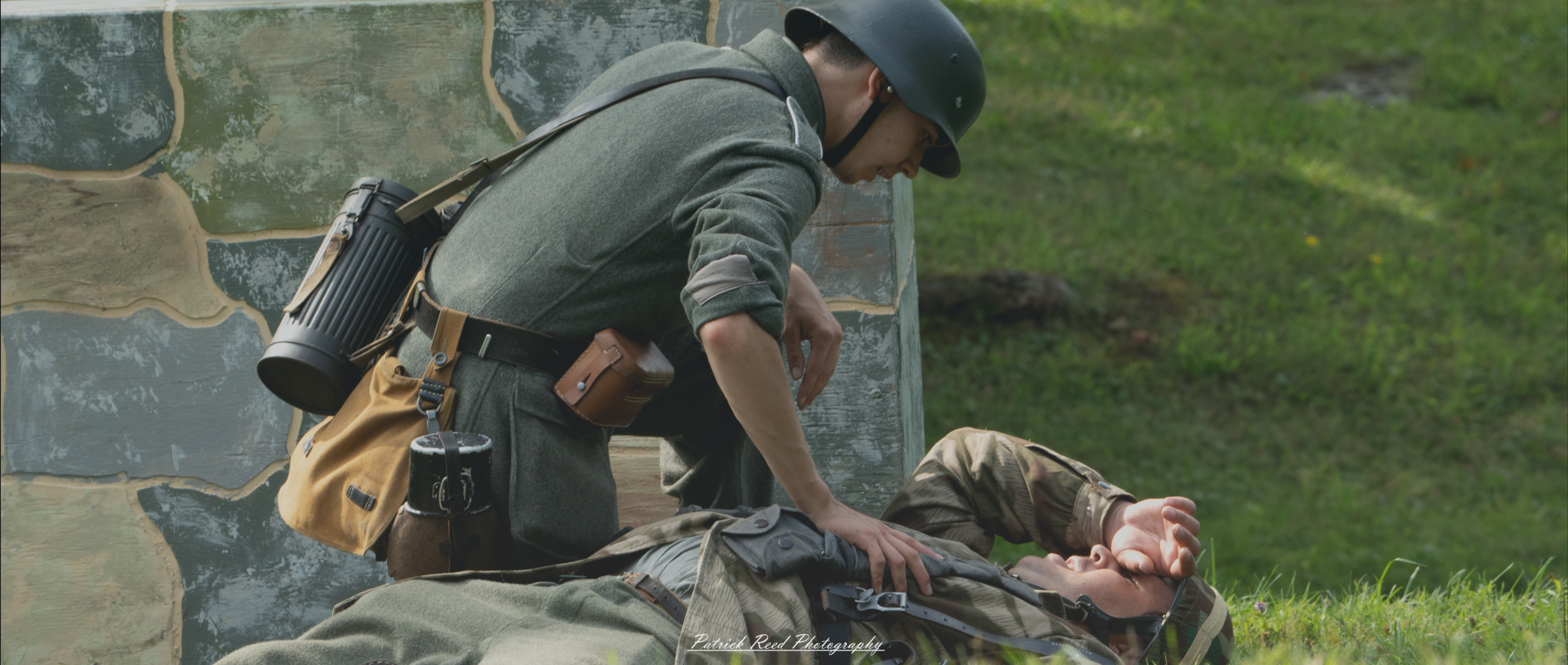 A poignant image of a German medic attending to a soldier lying on his back in a field. The medic is focused on providing care, illustrating the urgency and compassion of battlefield medicine during World War II in a moment of crisis.