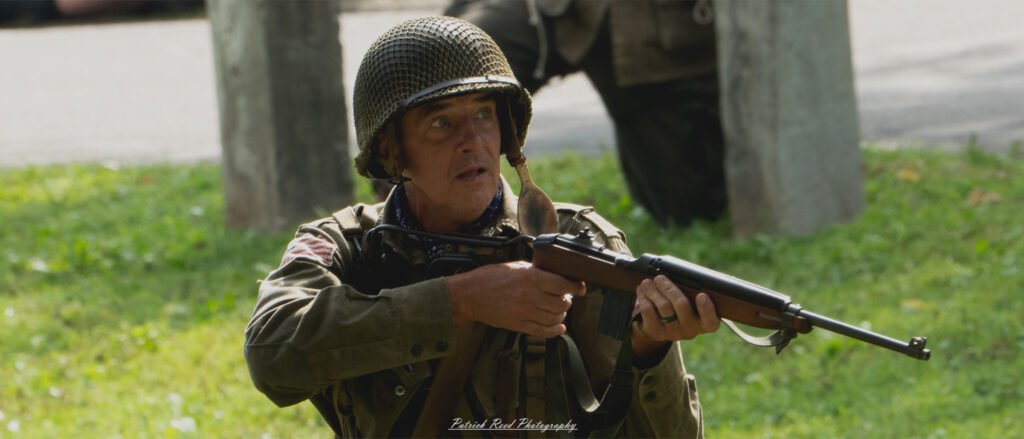 A paratrooper holding an M1 carbine, poised and alert in a dynamic setting. Dressed in full military gear, the soldier's focused expression and ready stance highlight the readiness and determination of airborne forces during combat.