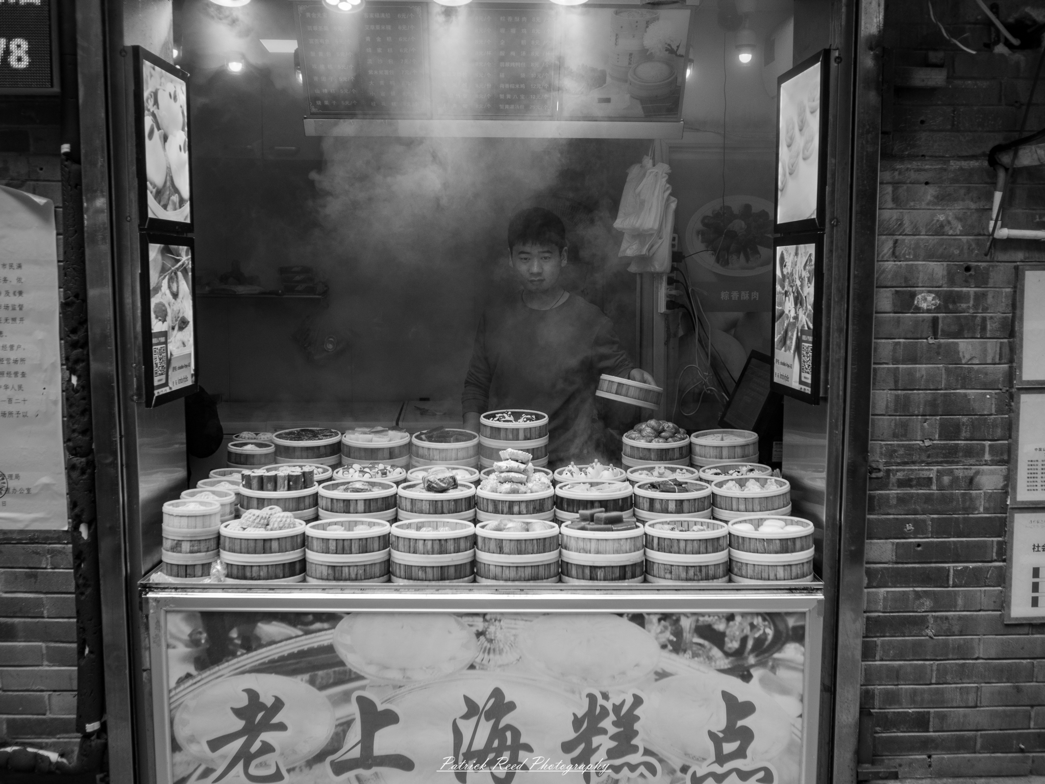China Food Vendor "A young man skillfully operates a food stall in China, surrounded by an array of delicious street food offerings. He is focused on preparing dishes, showcasing his culinary expertise, while vibrant ingredients and colorful food items fill the stall. The bustling atmosphere captures the lively essence of street food culture, with patrons eagerly waiting to sample the delights. The scene reflects the rich flavors and traditions of Chinese cuisine, highlighting the energetic vibe of local markets."