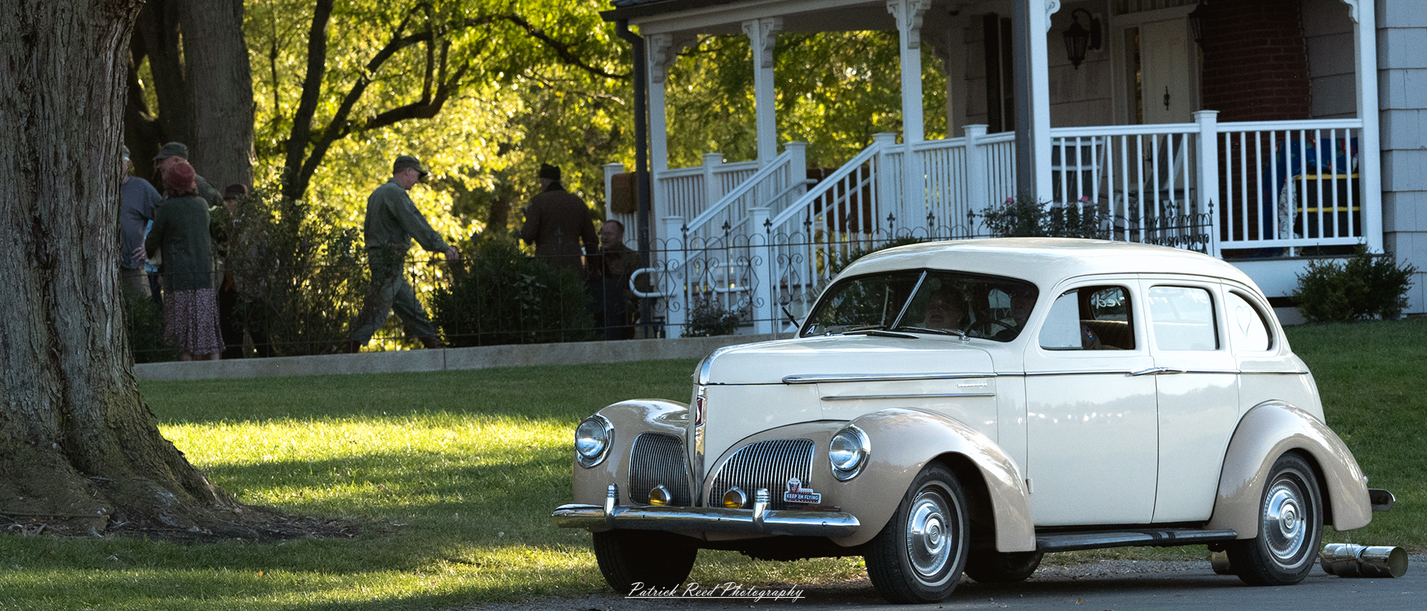 "Image of a vintage white Studebaker parked in front of a charming house, showcasing classic automotive design against a picturesque residential backdrop. The Studebaker gleams in the sunlight, highlighting its sleek lines and distinctive features. The house behind it, possibly featuring a well-manicured lawn and flowering shrubs, adds to the nostalgic ambiance of the scene. This combination captures a moment in time, evoking a sense of Americana and the allure of classic cars."