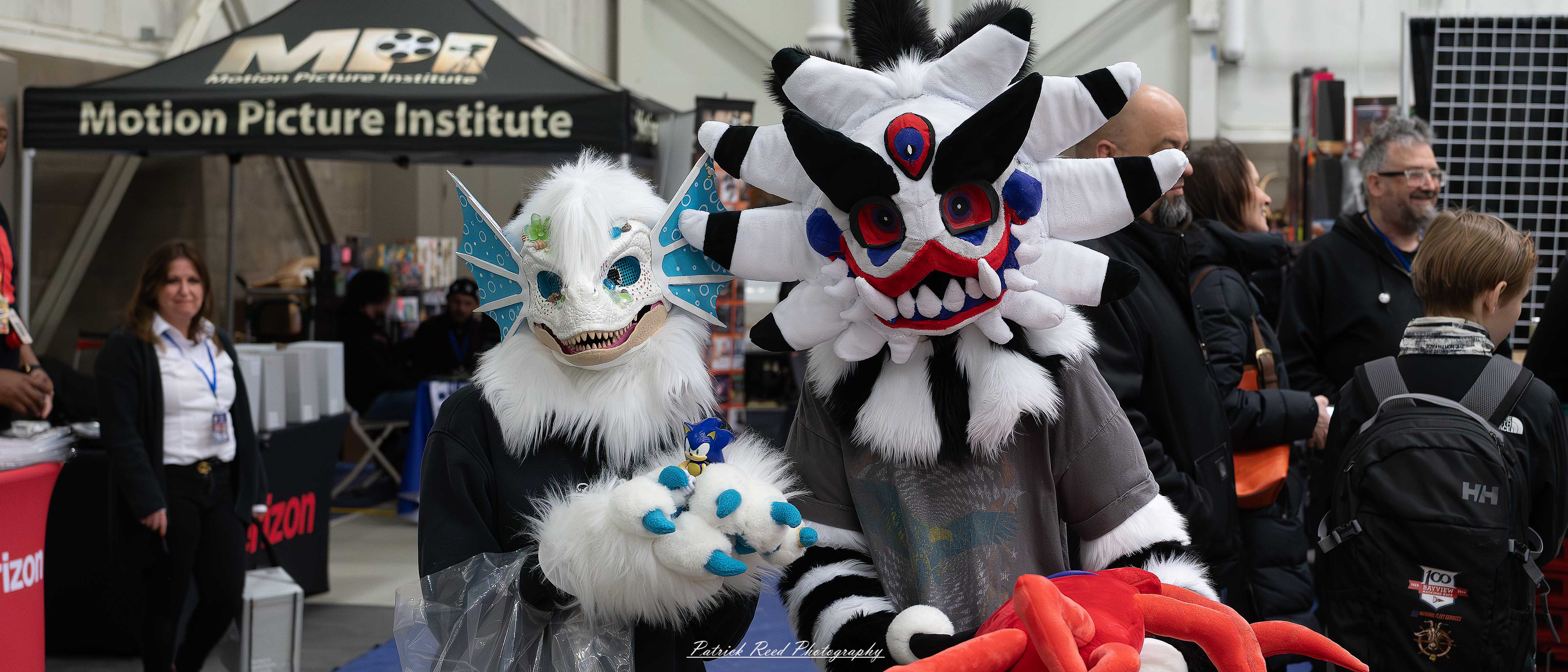 Great Lakes Comic Con 13 Alt text: A group of cosplayers posing on stage at the Great Lakes Comic Con cosplay contest, dressed as various characters from comics, anime, and video games. The audience watches from below as the participants show off their detailed costumes under bright stage lights.