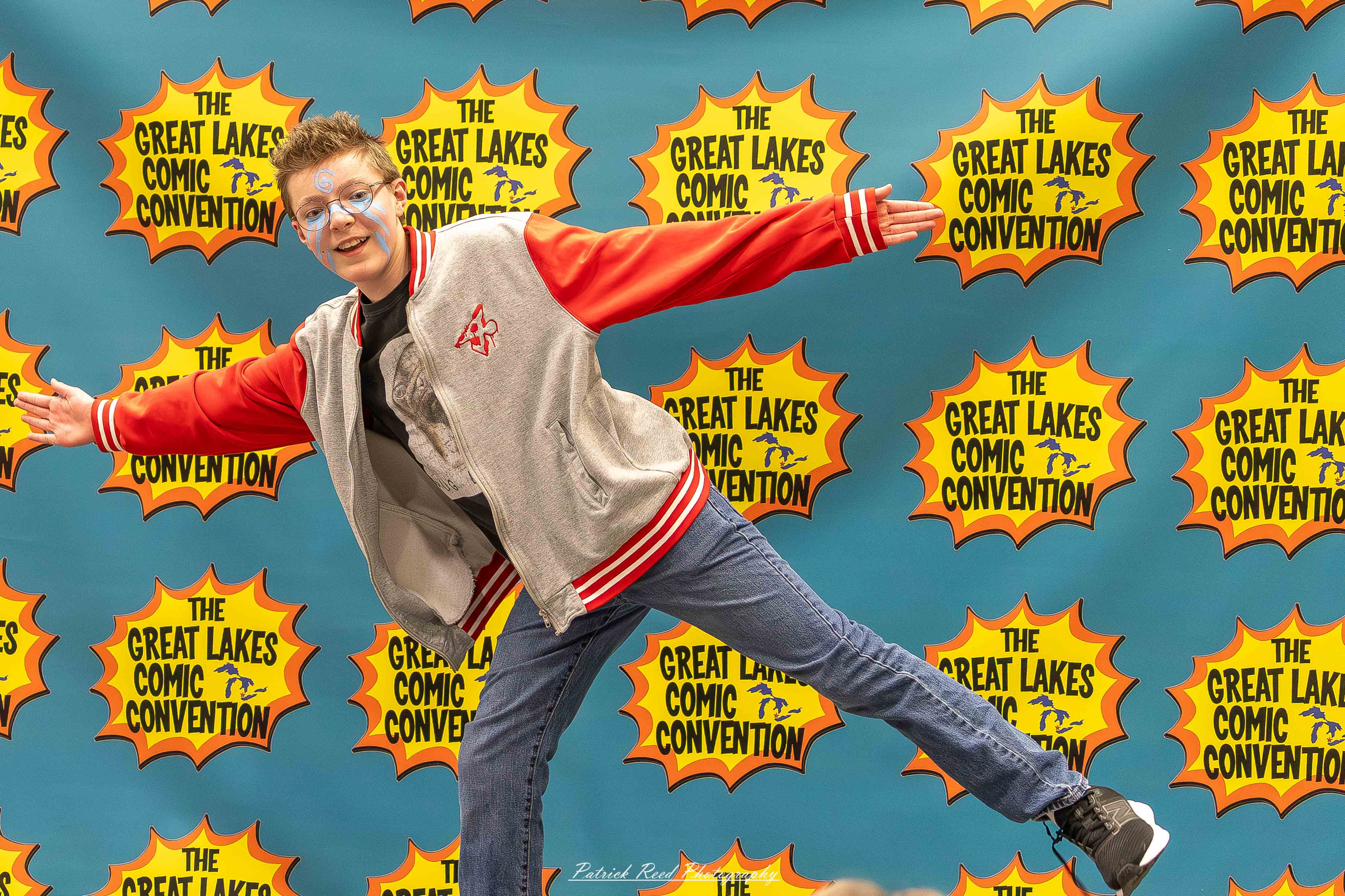 Great Lakes Comic Con 22 Alt text: A group of cosplayers posing on stage at the Great Lakes Comic Con cosplay contest, dressed as various characters from comics, anime, and video games. The audience watches from below as the participants show off their detailed costumes under bright stage lights.