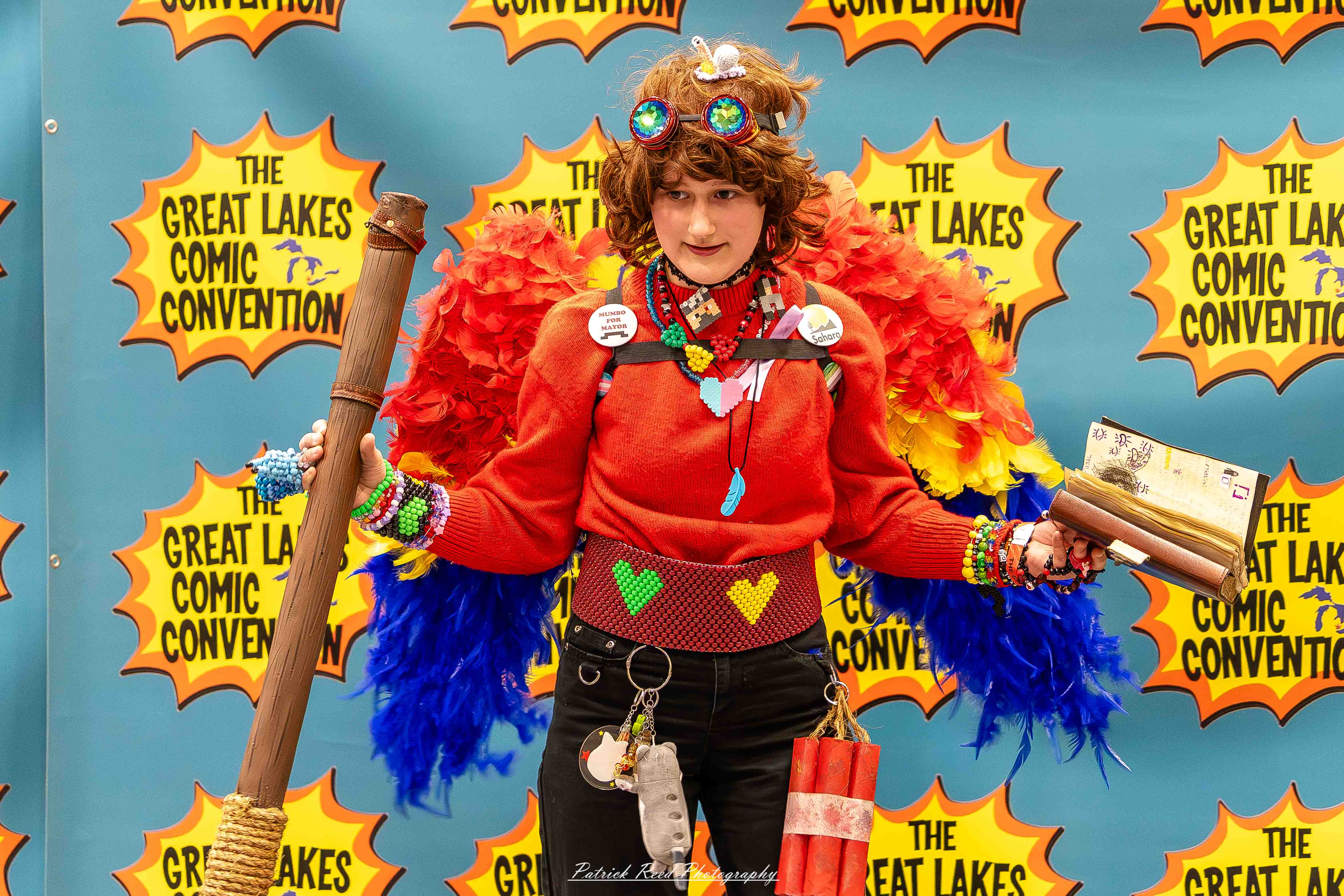 Great Lakes Comic Con 26 Alt text: A group of cosplayers posing on stage at the Great Lakes Comic Con cosplay contest, dressed as various characters from comics, anime, and video games. The audience watches from below as the participants show off their detailed costumes under bright stage lights.