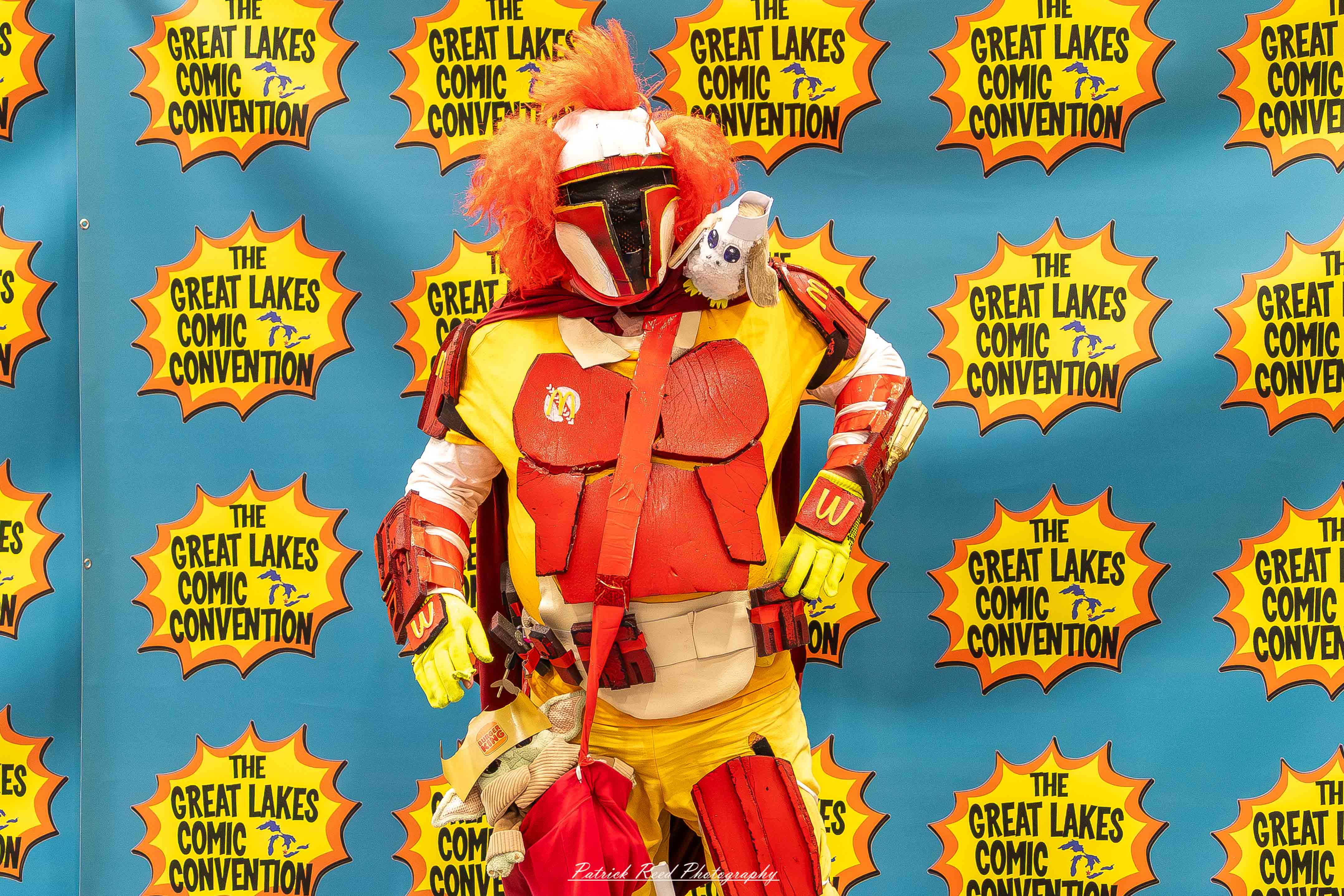 Great Lakes Comic Con 28 Alt text: A group of cosplayers posing on stage at the Great Lakes Comic Con cosplay contest, dressed as various characters from comics, anime, and video games. The audience watches from below as the participants show off their detailed costumes under bright stage lights.