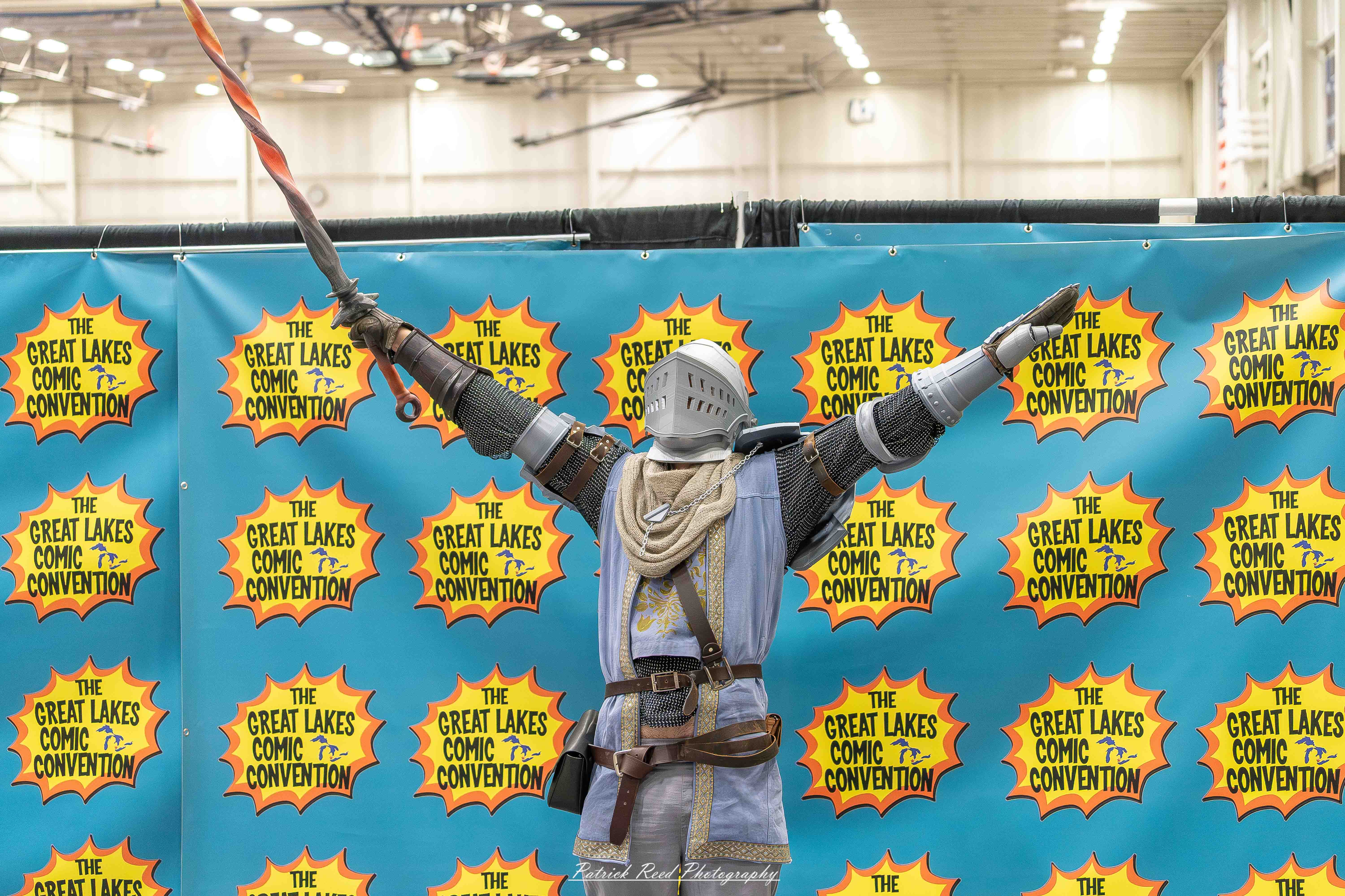 Great Lakes Comic Con 29 Alt text: A group of cosplayers posing on stage at the Great Lakes Comic Con cosplay contest, dressed as various characters from comics, anime, and video games. The audience watches from below as the participants show off their detailed costumes under bright stage lights.