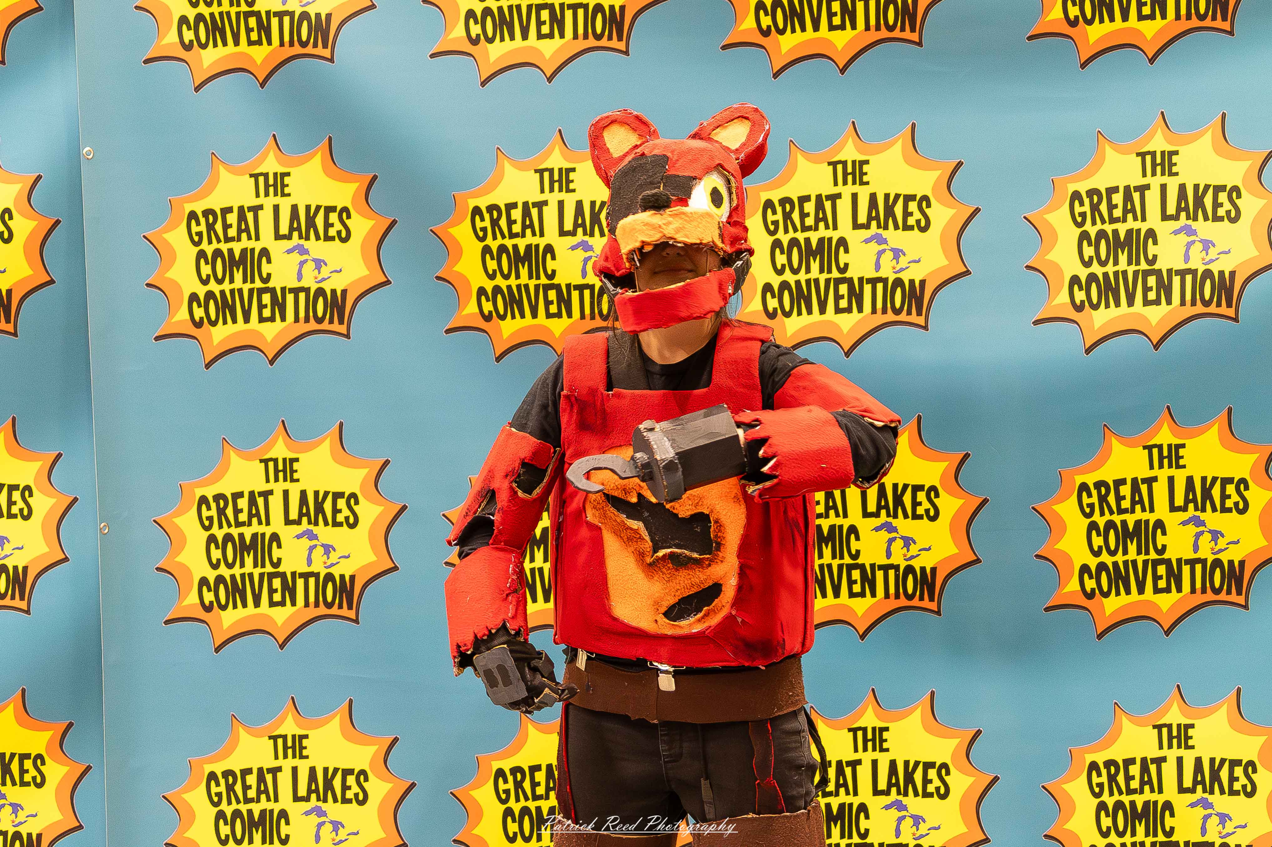 Great Lakes Comic Con 36 Alt text: A group of cosplayers posing on stage at the Great Lakes Comic Con cosplay contest, dressed as various characters from comics, anime, and video games. The audience watches from below as the participants show off their detailed costumes under bright stage lights.