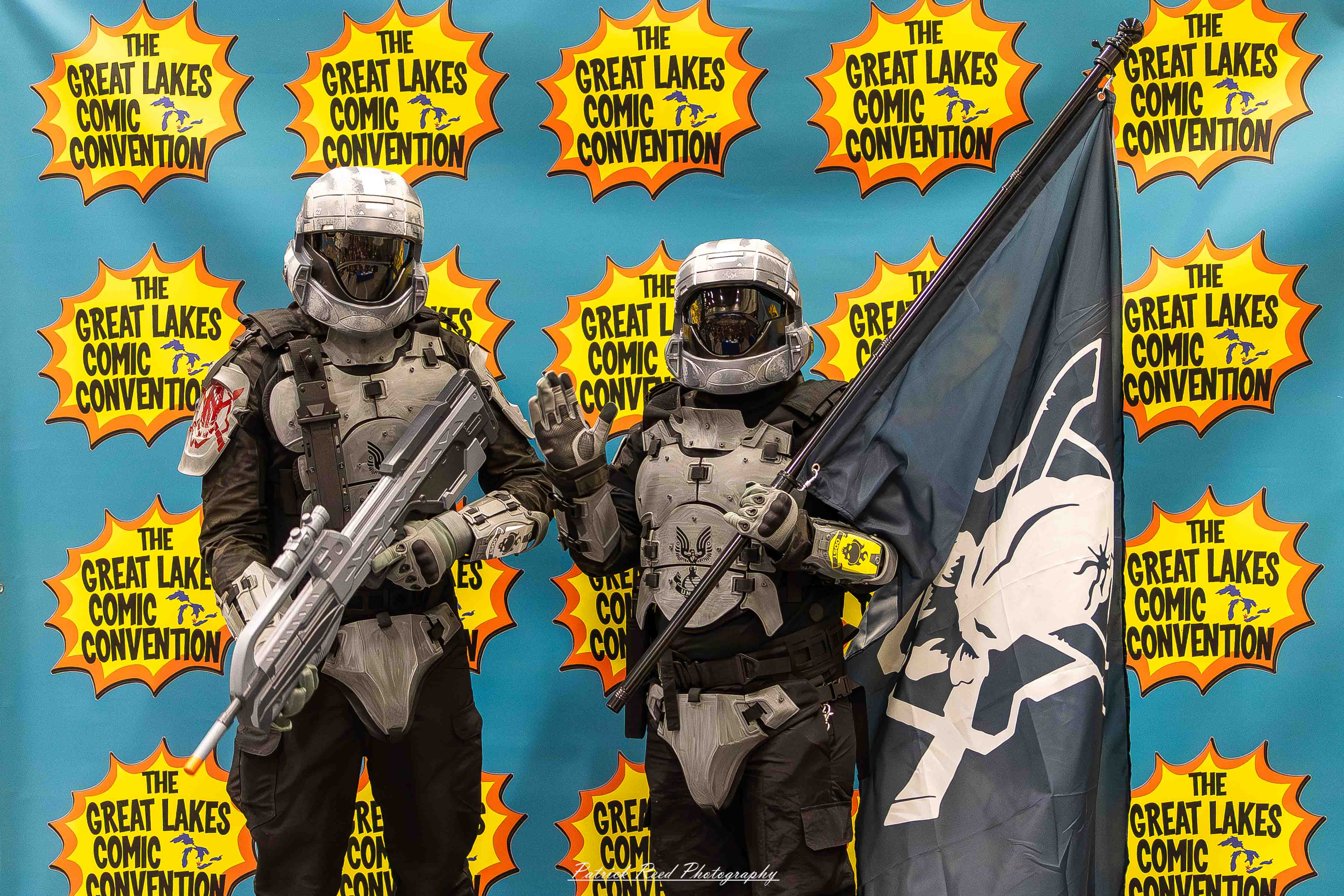 Great Lakes Comic Con 37 Alt text: A group of cosplayers posing on stage at the Great Lakes Comic Con cosplay contest, dressed as various characters from comics, anime, and video games. The audience watches from below as the participants show off their detailed costumes under bright stage lights.