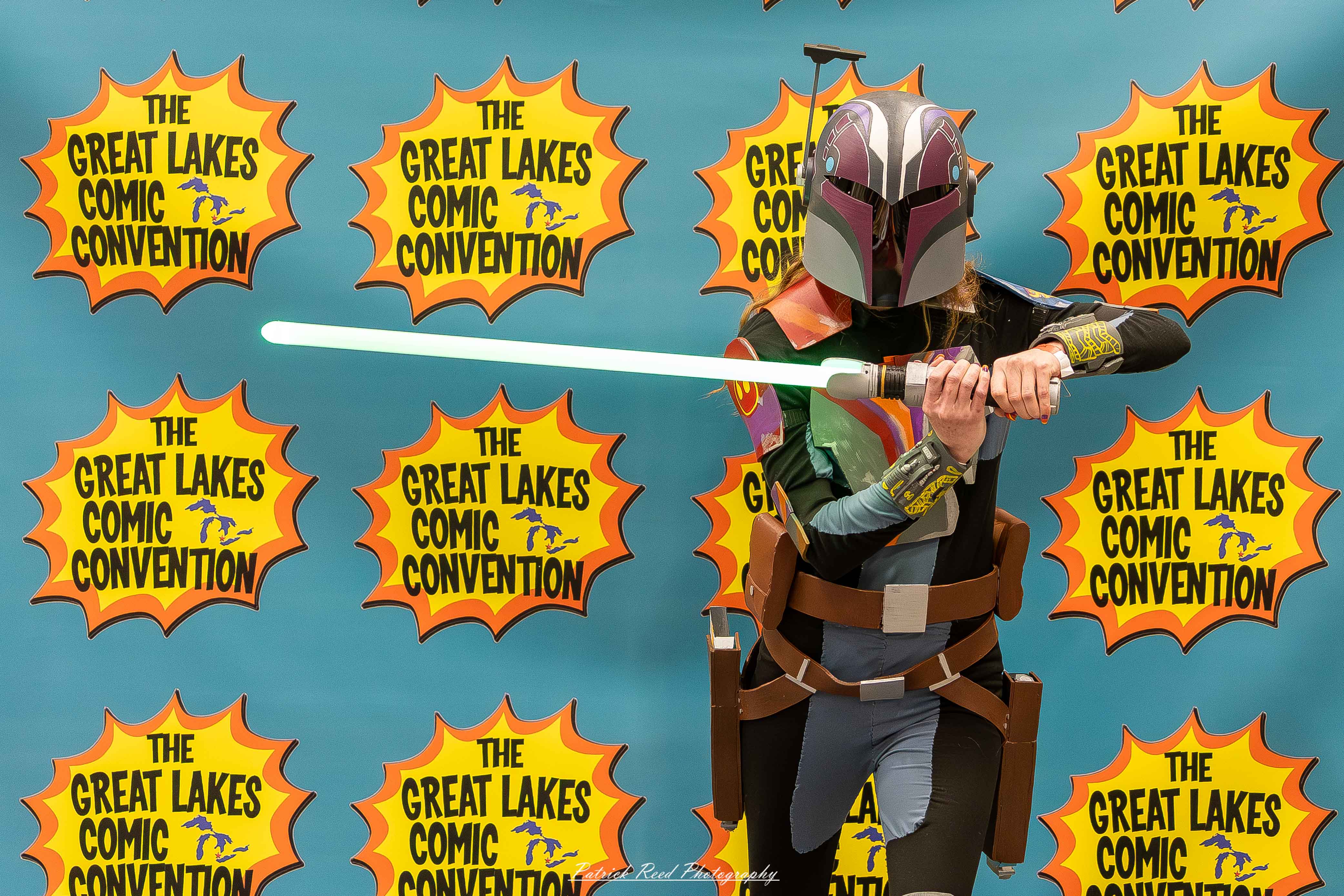 Great Lakes Comic Con 38 Alt text: A group of cosplayers posing on stage at the Great Lakes Comic Con cosplay contest, dressed as various characters from comics, anime, and video games. The audience watches from below as the participants show off their detailed costumes under bright stage lights.