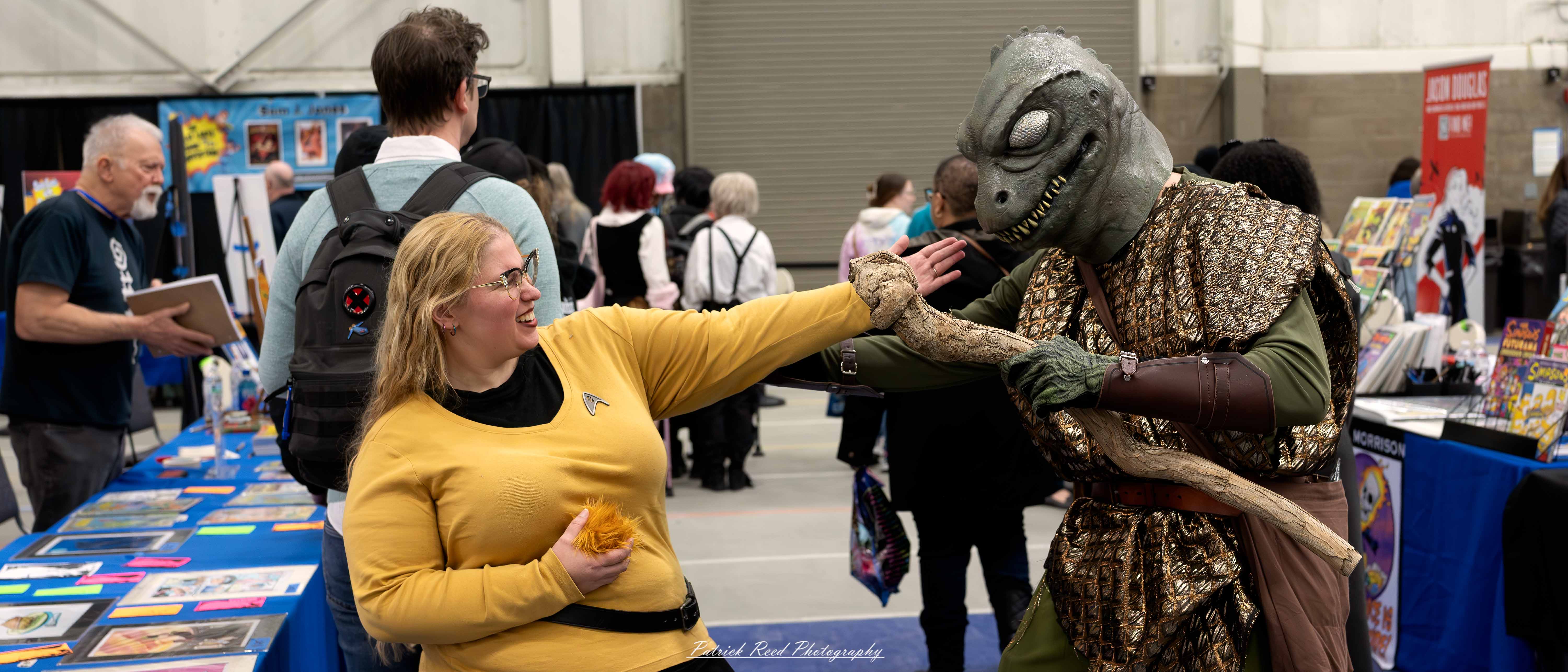 Great Lakes Comic Con 4 wo cosplayers dressed as Captain Kirk and the Gorn from Star Trek pose at the Great Lakes Comic Con cosplay contest. Captain Kirk wears a classic gold Starfleet uniform with black pants and boots, striking a heroic pose. Beside him, the Gorn cosplayer dons a reptilian mask and scaly green costume with a tan tunic, recreating the iconic showdown.