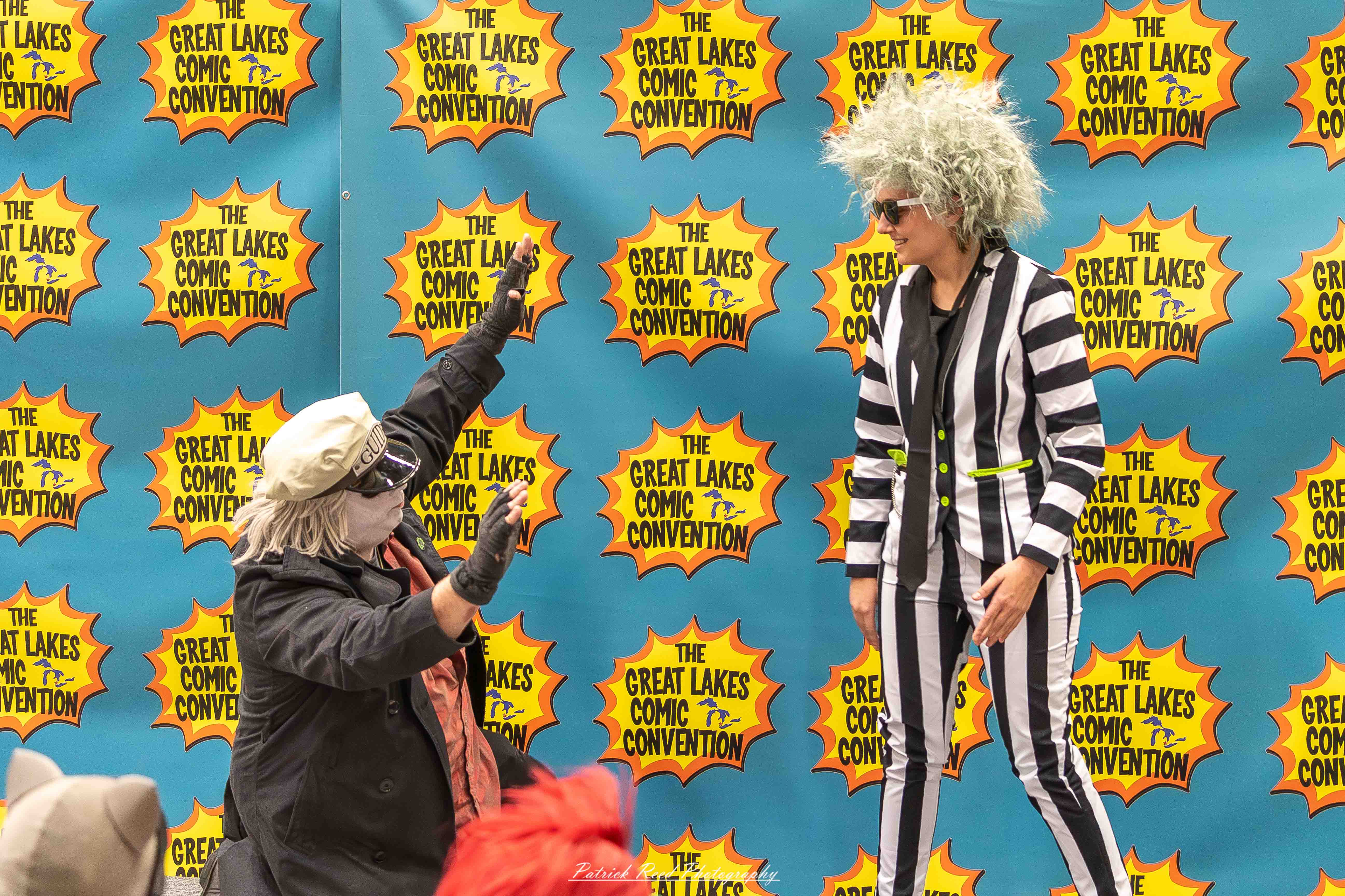 Great Lakes Comic Con 45 Alt text: A group of cosplayers posing on stage at the Great Lakes Comic Con cosplay contest, dressed as various characters from comics, anime, and video games. The audience watches from below as the participants show off their detailed costumes under bright stage lights.