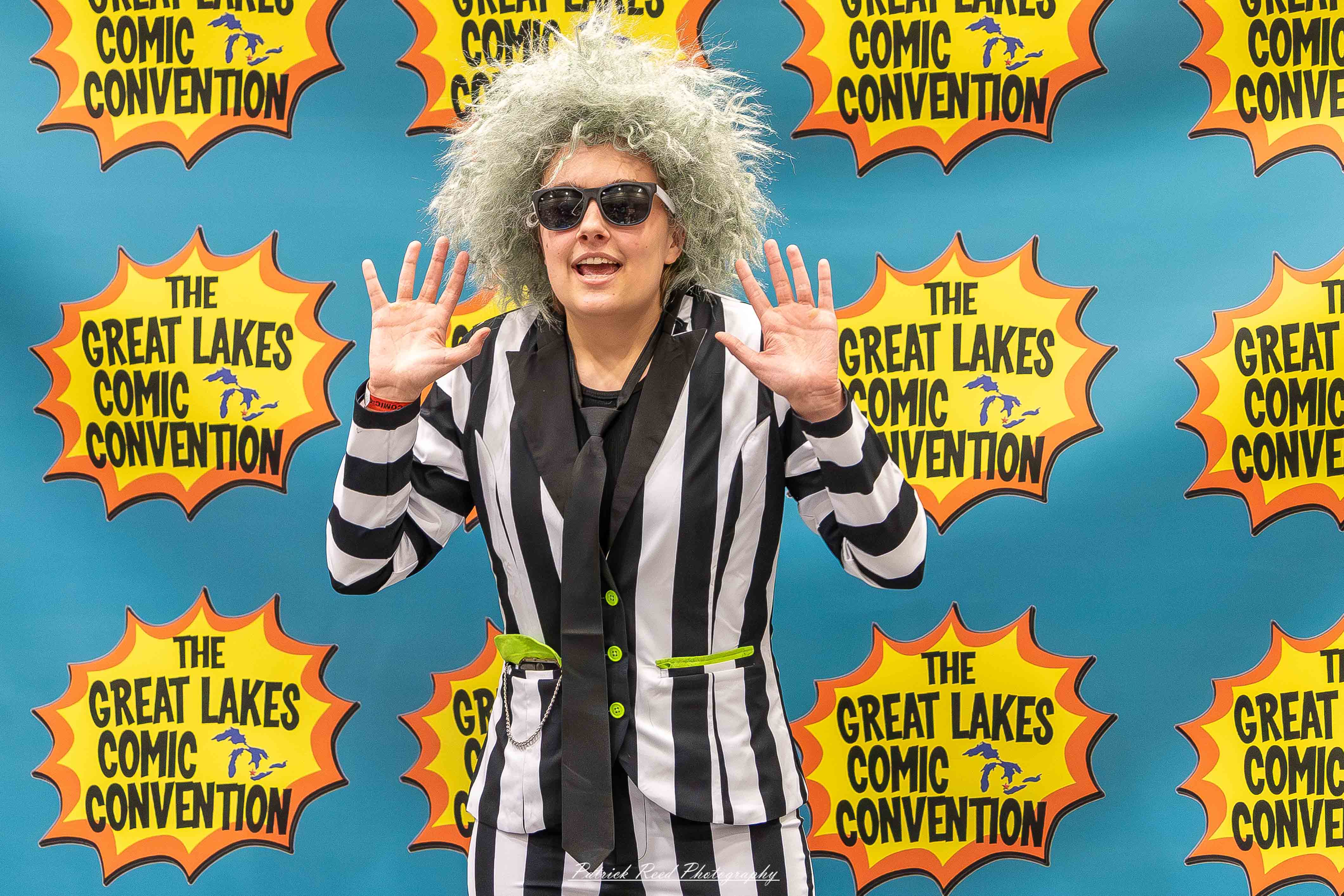 Great Lakes Comic Con 46 Alt text: A group of cosplayers posing on stage at the Great Lakes Comic Con cosplay contest, dressed as various characters from comics, anime, and video games. The audience watches from below as the participants show off their detailed costumes under bright stage lights.