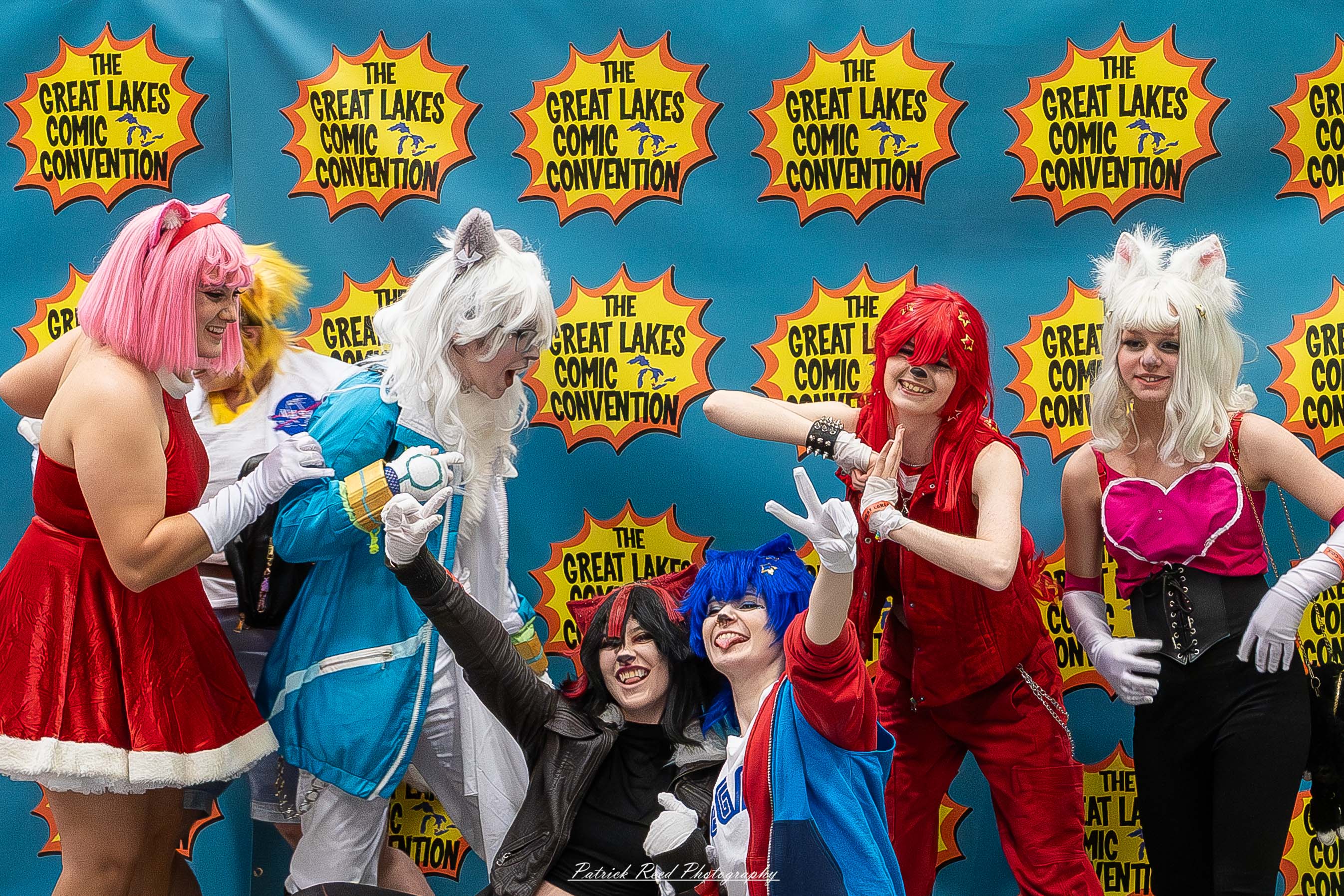 Great Lakes Comic Con 49 Alt text: A group of cosplayers posing on stage at the Great Lakes Comic Con cosplay contest, dressed as various characters from comics, anime, and video games. The audience watches from below as the participants show off their detailed costumes under bright stage lights.