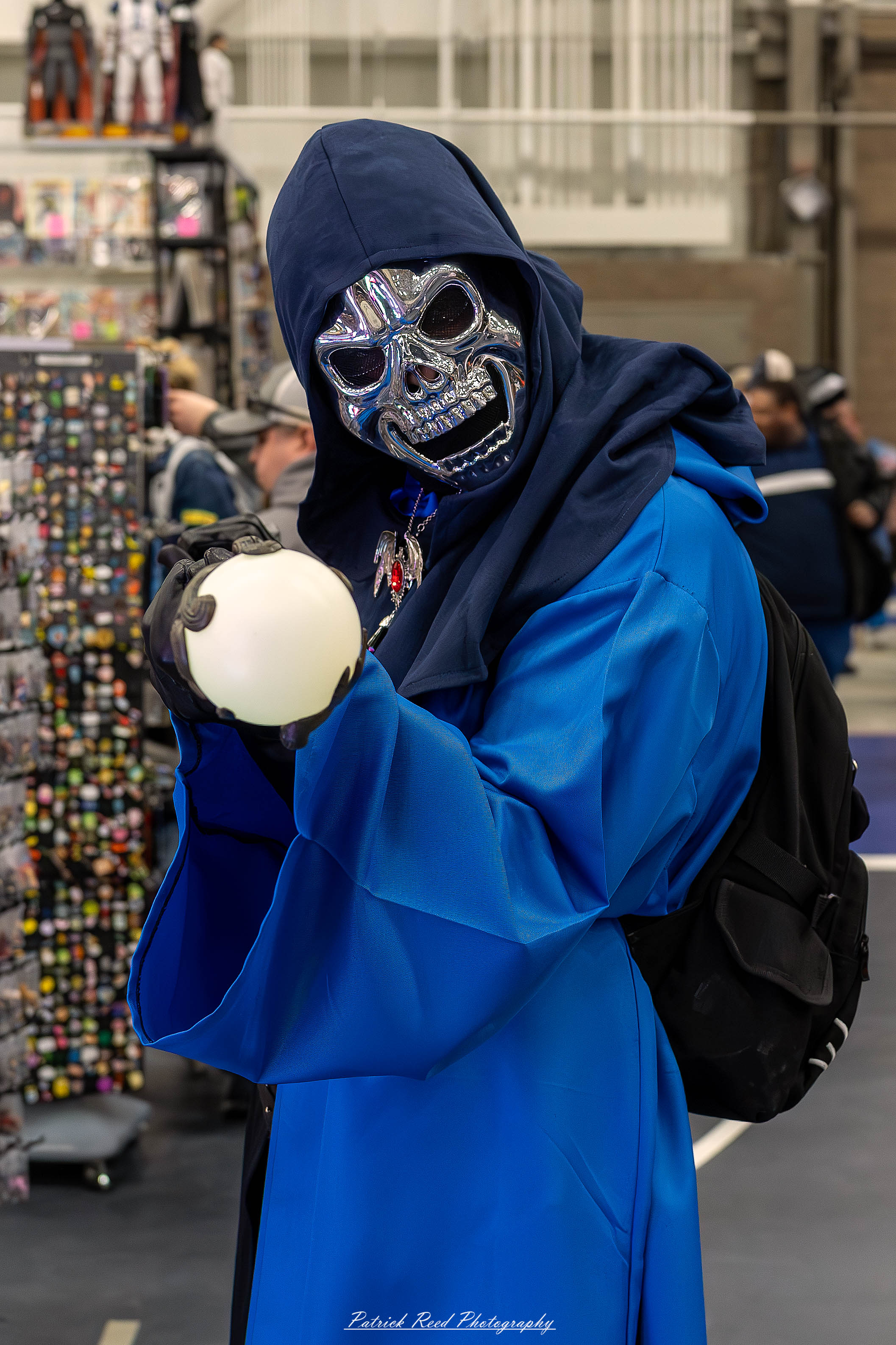 Great Lakes Comic Con 6 A cosplayer dressed as Skeletor from Masters of the Universe poses at the Great Lakes Comic Con cosplay contest. They wear a blue bodysuit with purple armor, a hooded cowl, and a skull mask. The cosplayer holds Skeletor’s iconic Havoc Staff topped with a ram’s skull,