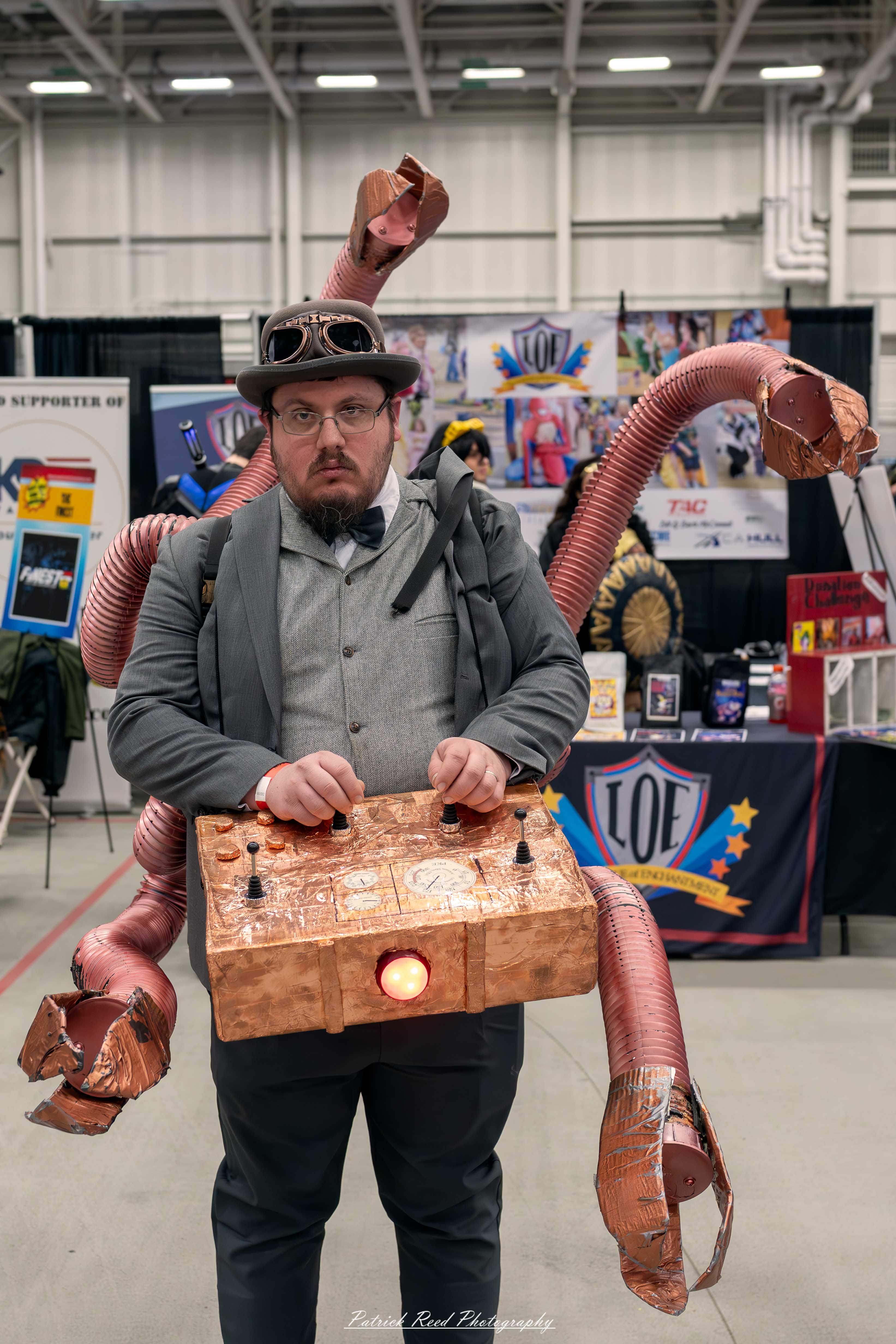 Great Lakes Comic Con 7 A cosplayer dressed as Doctor Octopus poses at the Great Lakes Comic Con cosplay contest. They wear a green jumpsuit with a yellow belt and gloves, along with four large mechanical tentacles extending from a harness on their back.
