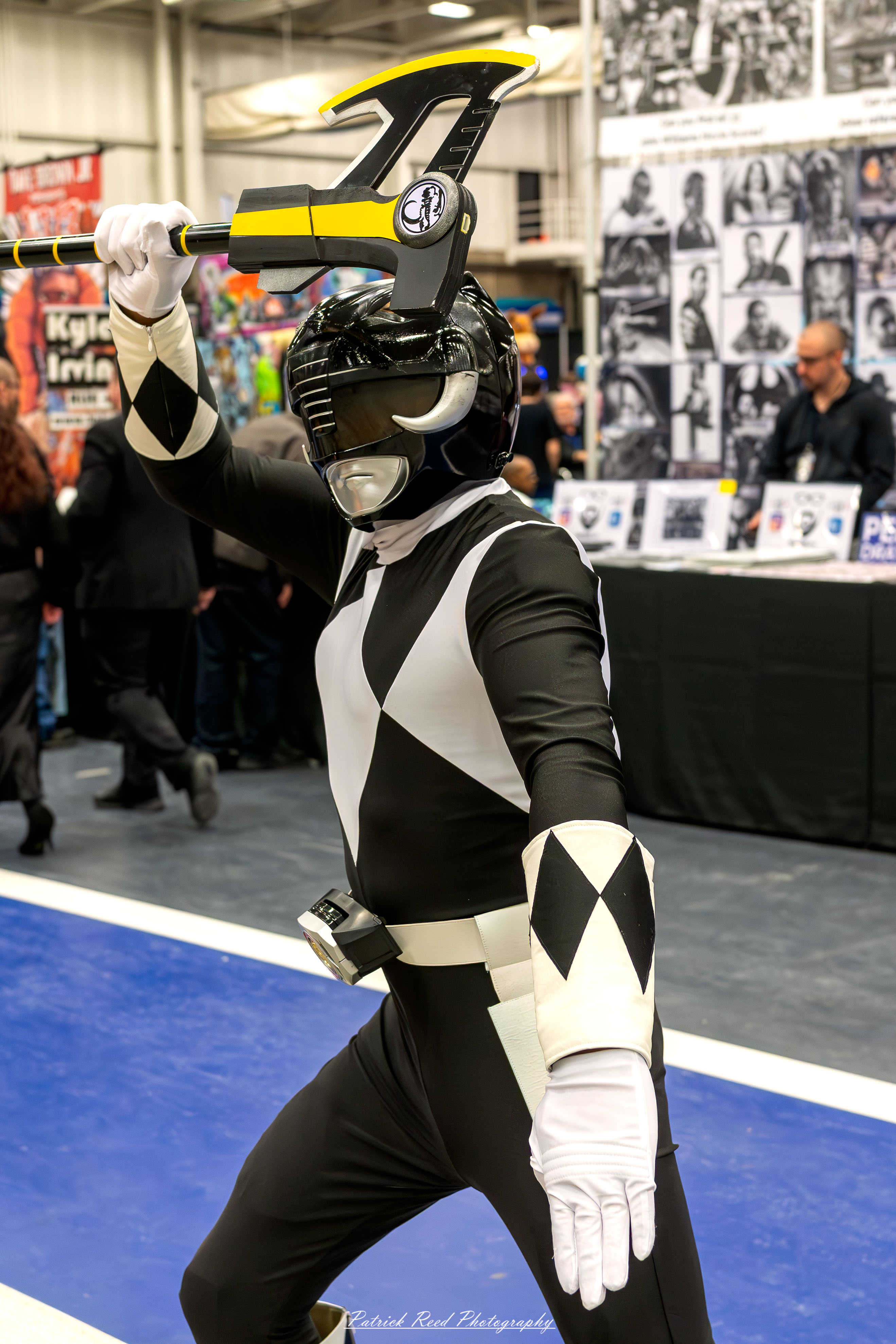 Great Lakes Comic Con 8 A cosplayer dressed as the Black Power Ranger poses confidently at the Great Lakes Comic Con cosplay contest. The costume features a sleek black and white spandex suit with a diamond-shaped chest pattern, a matching helmet with a black visor, and a Power Morpher belt.