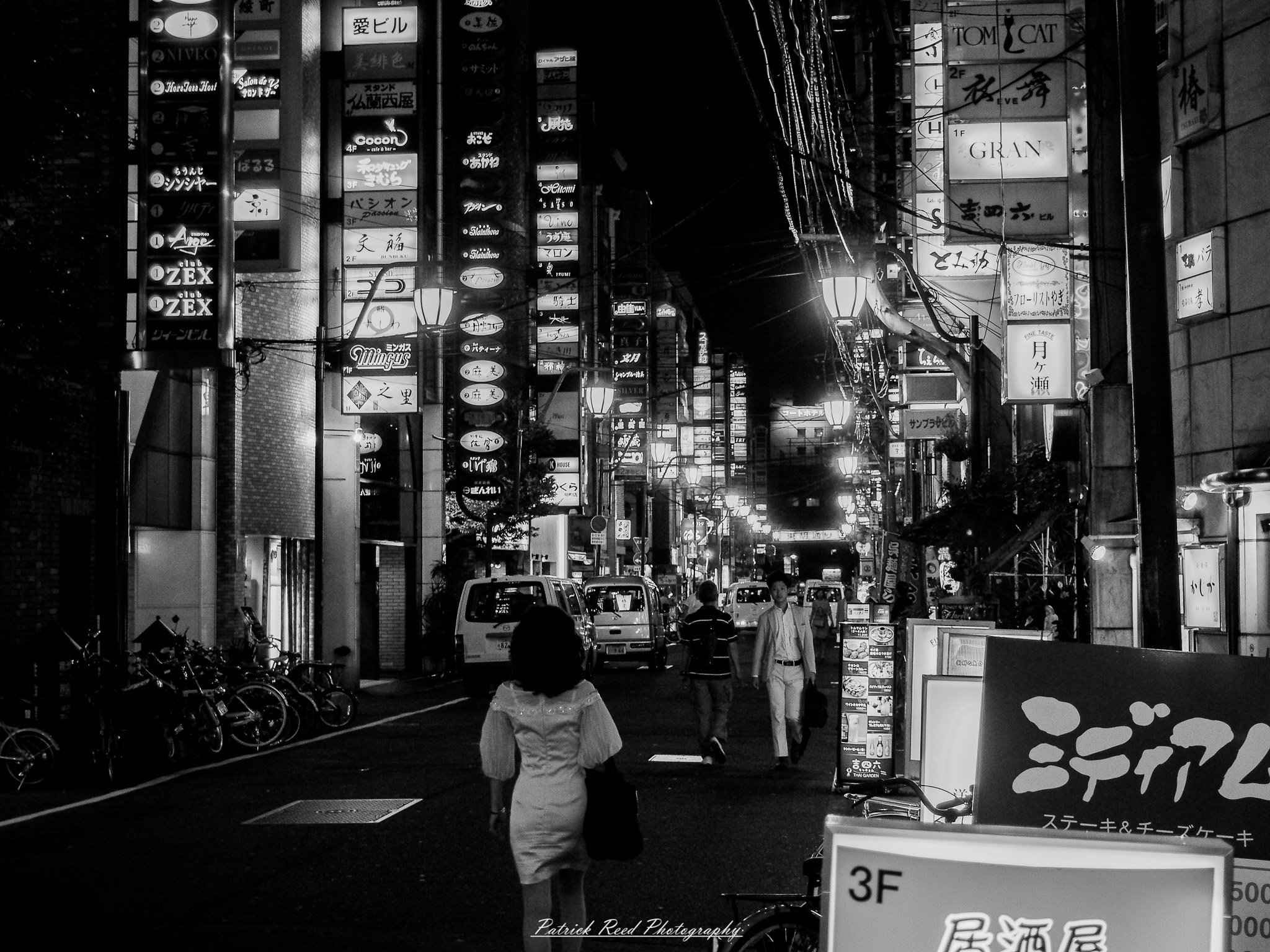 A series of noir-style street photography scenes set in Hiroshima, Japan, at night. The rain-slicked streets and narrow alleys reflect the soft glow of neon signs from izakayas, small shops, and vending machines. Silhouettes of people walking under umbrellas move through the misty atmosphere, their shadows stretching across the pavement. Traditional Japanese architecture, such as wooden facades and noren curtains, blends with modern urban elements like glowing billboards and bicycles parked along dimly lit sidewalks. The moody lighting, deep contrasts, and quiet yet cinematic ambiance evoke a sense of mystery and nostalgia, capturing the noir aesthetic in a contemporary Japanese cityscape.