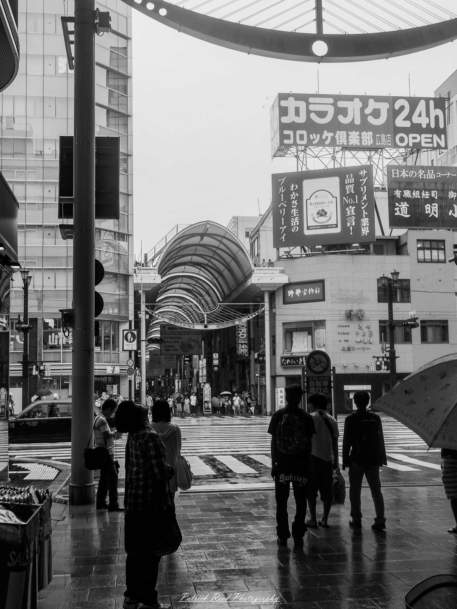 A series of noir-style street photography scenes set in Hiroshima, Japan, at night. The rain-slicked streets and narrow alleys reflect the soft glow of neon signs from izakayas, small shops, and vending machines. Silhouettes of people walking under umbrellas move through the misty atmosphere, their shadows stretching across the pavement. Traditional Japanese architecture, such as wooden facades and noren curtains, blends with modern urban elements like glowing billboards and bicycles parked along dimly lit sidewalks. The moody lighting, deep contrasts, and quiet yet cinematic ambiance evoke a sense of mystery and nostalgia, capturing the noir aesthetic in a contemporary Japanese cityscape.