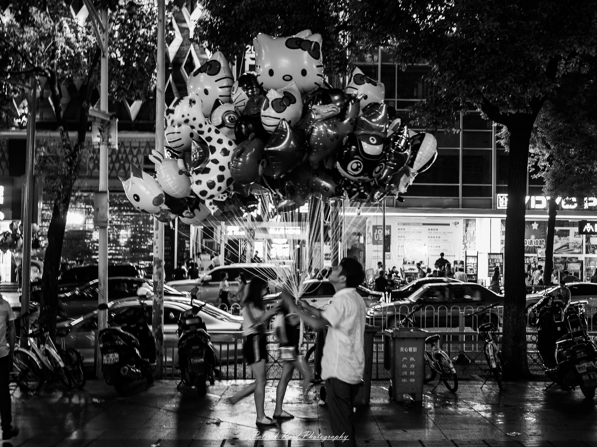 China Noir Scene 5 A noir-style scene of a narrow alley in China at night, with wet cobblestone pavement reflecting neon lights from signs and windows. A scooter is parked against a wall, partially illuminated by the glow of a flickering sign. The alley is framed by traditional Chinese architectural details, such as tiled roofs and lanterns, blending with urban elements like graffiti and wires. Silhouettes of people holding umbrellas walk through the misty atmosphere in the background, adding a sense of mystery and storytelling. The overall mood is cinematic, gritty, and evocative.