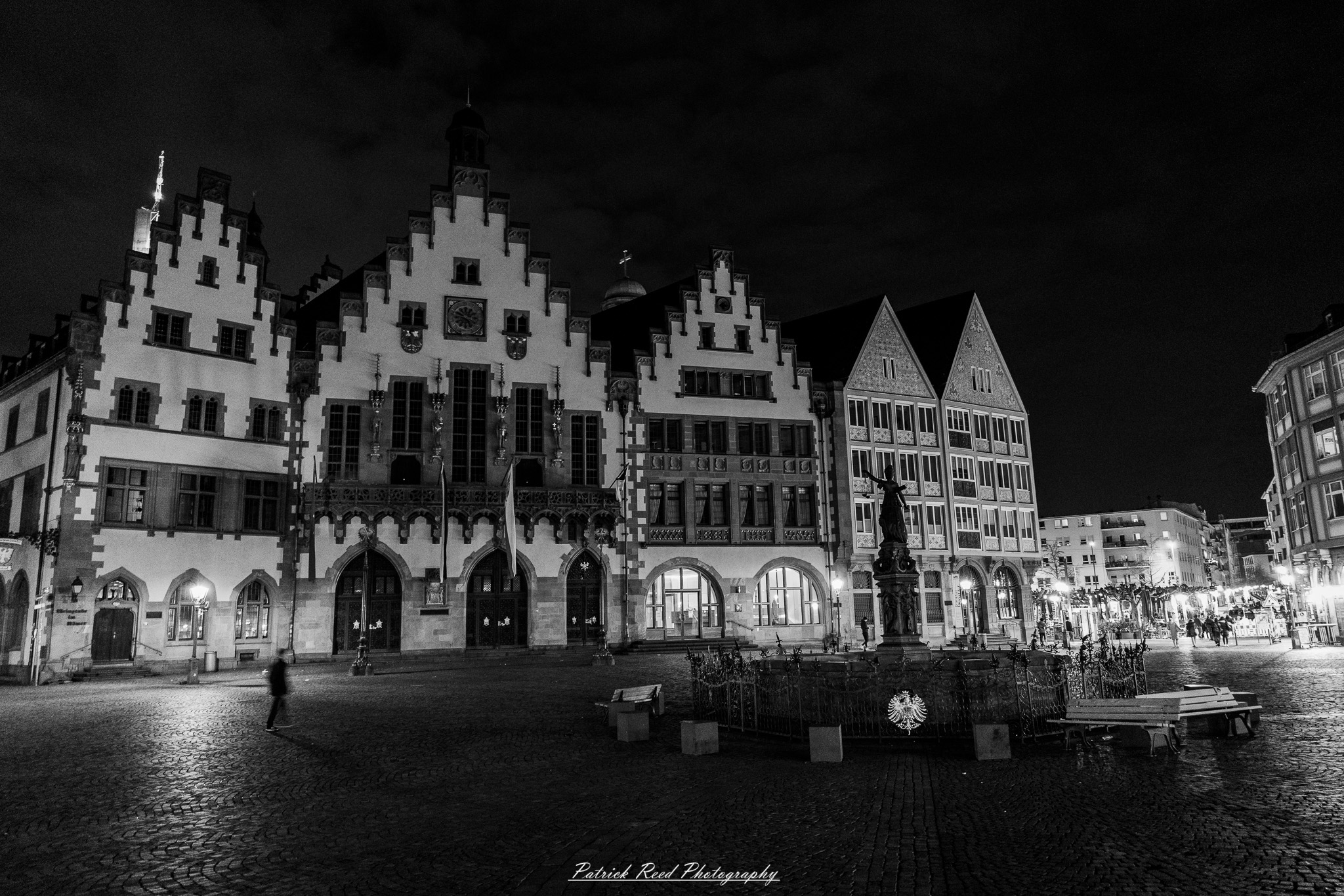 Russelsheim 15 A series of noir-style street photography scenes set in Rüsselsheim, Germany, at night. The dimly lit streets feature wet cobblestones reflecting the glow of streetlights and neon signs. Shadows and silhouettes of people, some walking or riding bicycles, add a mysterious atmosphere. Industrial architecture, such as factory buildings and modern urban structures, contrasts with old-world charm. Elements like parked cars, lampposts, and occasional graffiti create a gritty, cinematic ambiance. The misty air and moody lighting emphasize the noir aesthetic, evoking a sense of intrigue and storytelling.