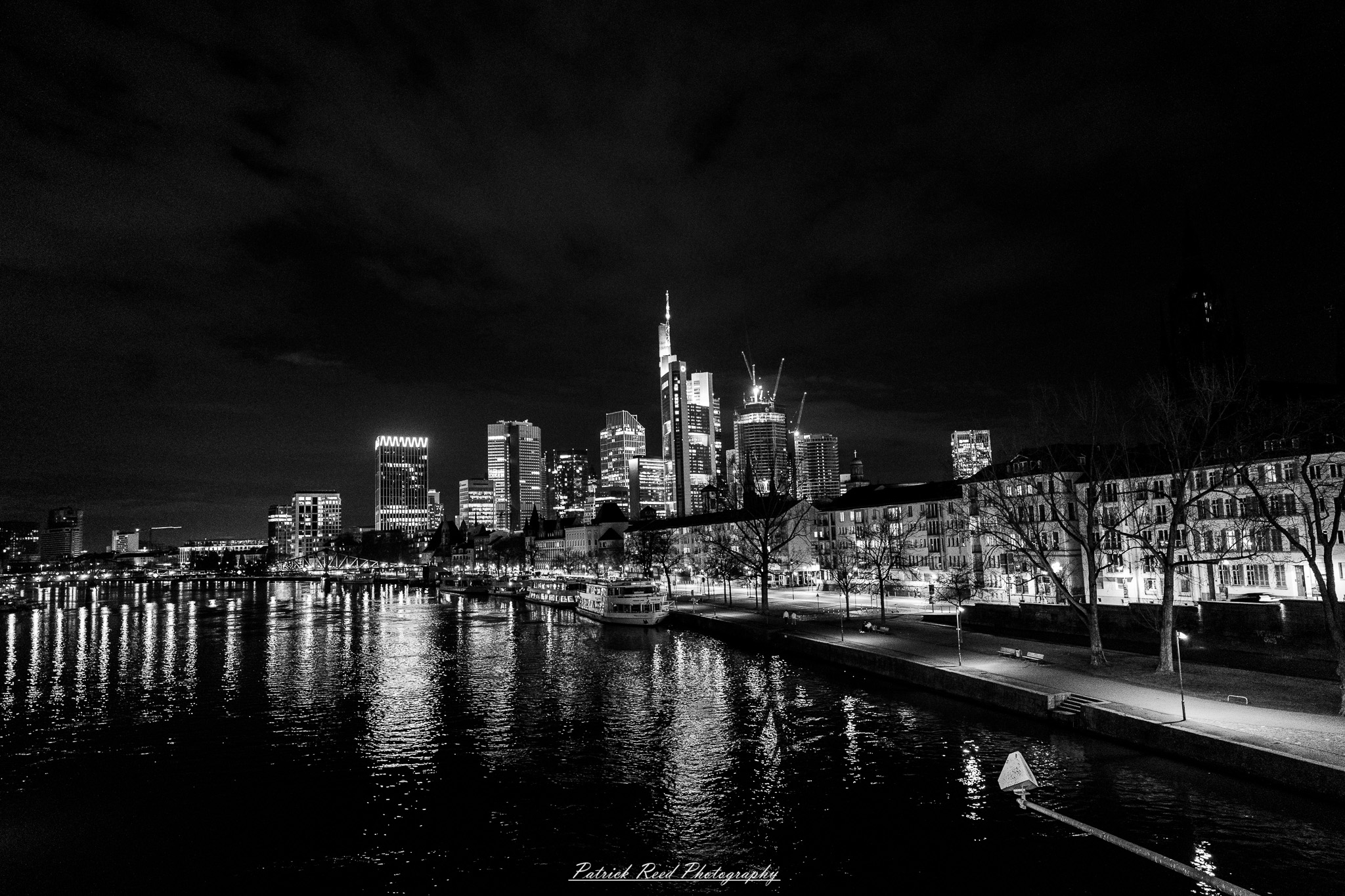 Russelsheim 17 A series of noir-style street photography scenes set in Rüsselsheim, Germany, at night. The dimly lit streets feature wet cobblestones reflecting the glow of streetlights and neon signs. Shadows and silhouettes of people, some walking or riding bicycles, add a mysterious atmosphere. Industrial architecture, such as factory buildings and modern urban structures, contrasts with old-world charm. Elements like parked cars, lampposts, and occasional graffiti create a gritty, cinematic ambiance. The misty air and moody lighting emphasize the noir aesthetic, evoking a sense of intrigue and storytelling.