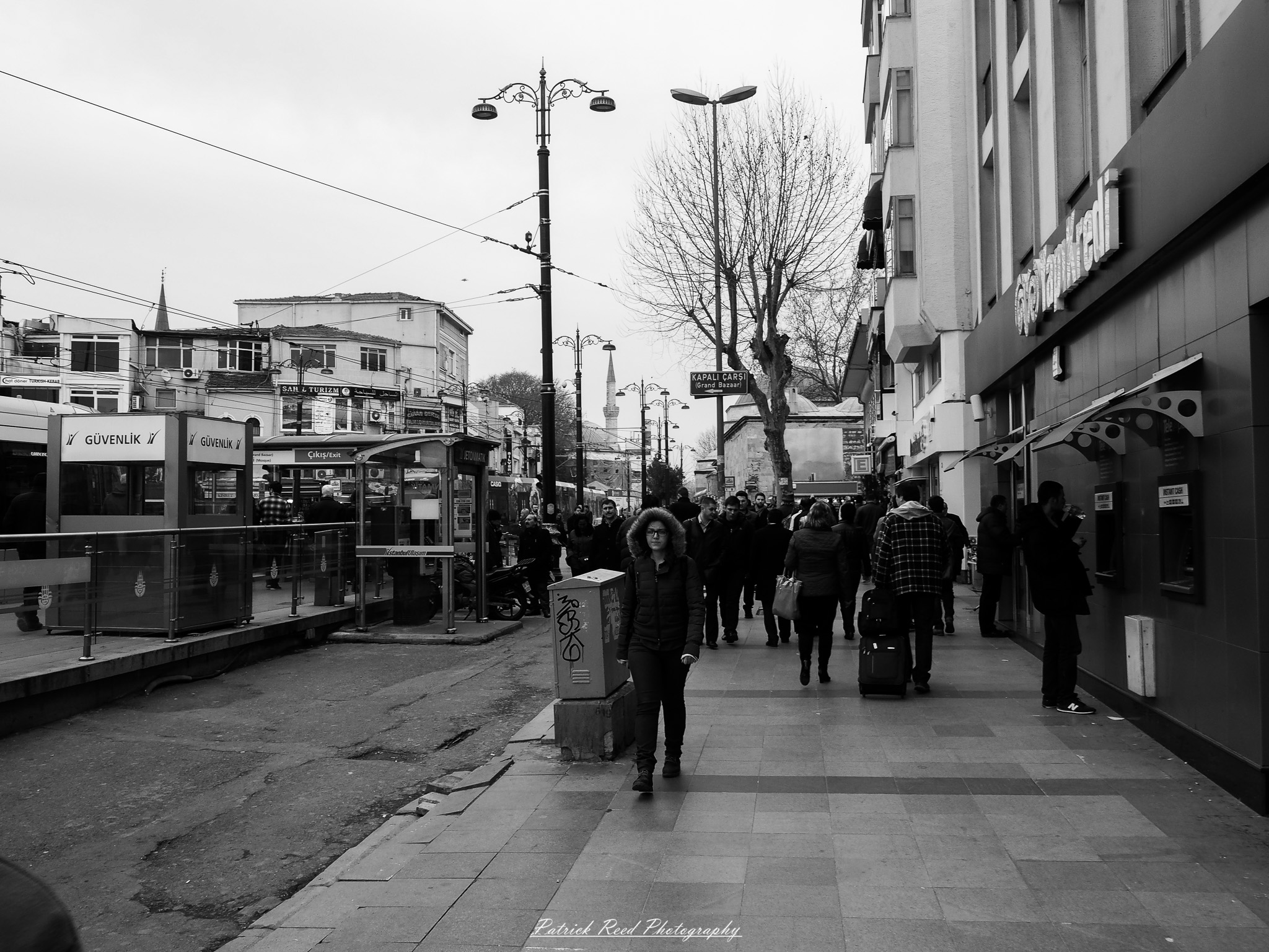 Turkey 10 A series of noir-style street photography scenes set in Istanbul, Turkey, at night. The dimly lit streets and narrow alleys are wet from rain, reflecting the warm glow of streetlights and neon signs. Silhouettes of people walking, some carrying umbrellas, move through the misty atmosphere. The scenes highlight a blend of historical Ottoman architecture, such as arched doorways and intricate stone facades, with modern urban elements like cafes, storefronts, and graffiti. The Bosphorus skyline and glimpses of minarets in the distance add to the cinematic, mysterious ambiance. The overall mood is evocative and steeped in noir storytelling.