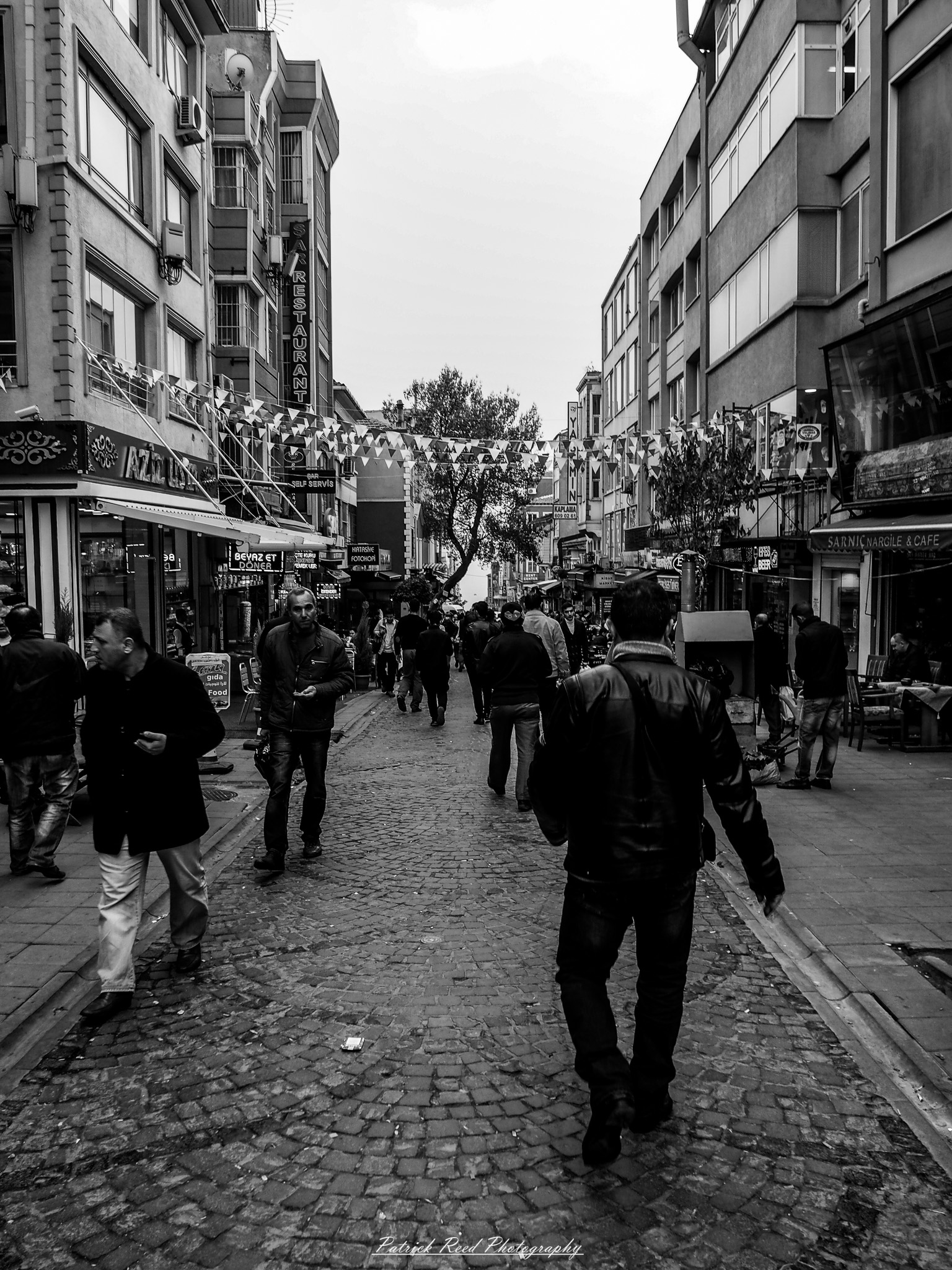 Turkey 11 A series of noir-style street photography scenes set in Istanbul, Turkey, at night. The dimly lit streets and narrow alleys are wet from rain, reflecting the warm glow of streetlights and neon signs. Silhouettes of people walking, some carrying umbrellas, move through the misty atmosphere. The scenes highlight a blend of historical Ottoman architecture, such as arched doorways and intricate stone facades, with modern urban elements like cafes, storefronts, and graffiti. The Bosphorus skyline and glimpses of minarets in the distance add to the cinematic, mysterious ambiance. The overall mood is evocative and steeped in noir storytelling.