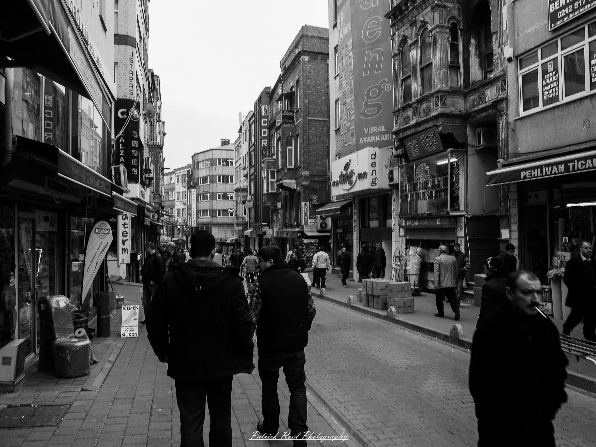 Turkey 12 A series of noir-style street photography scenes set in Istanbul, Turkey, at night. The dimly lit streets and narrow alleys are wet from rain, reflecting the warm glow of streetlights and neon signs. Silhouettes of people walking, some carrying umbrellas, move through the misty atmosphere. The scenes highlight a blend of historical Ottoman architecture, such as arched doorways and intricate stone facades, with modern urban elements like cafes, storefronts, and graffiti. The Bosphorus skyline and glimpses of minarets in the distance add to the cinematic, mysterious ambiance. The overall mood is evocative and steeped in noir storytelling.