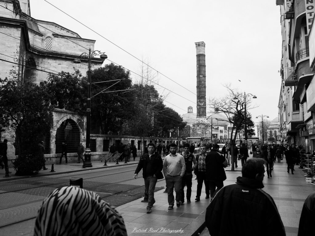 A series of noir-style street photography scenes set in Istanbul, Turkey, at night. The dimly lit streets and narrow alleys are wet from rain, reflecting the warm glow of streetlights and neon signs. Silhouettes of people walking, some carrying umbrellas, move through the misty atmosphere. The scenes highlight a blend of historical Ottoman architecture, such as arched doorways and intricate stone facades, with modern urban elements like cafes, storefronts, and graffiti. The Bosphorus skyline and glimpses of minarets in the distance add to the cinematic, mysterious ambiance. The overall mood is evocative and steeped in noir storytelling.