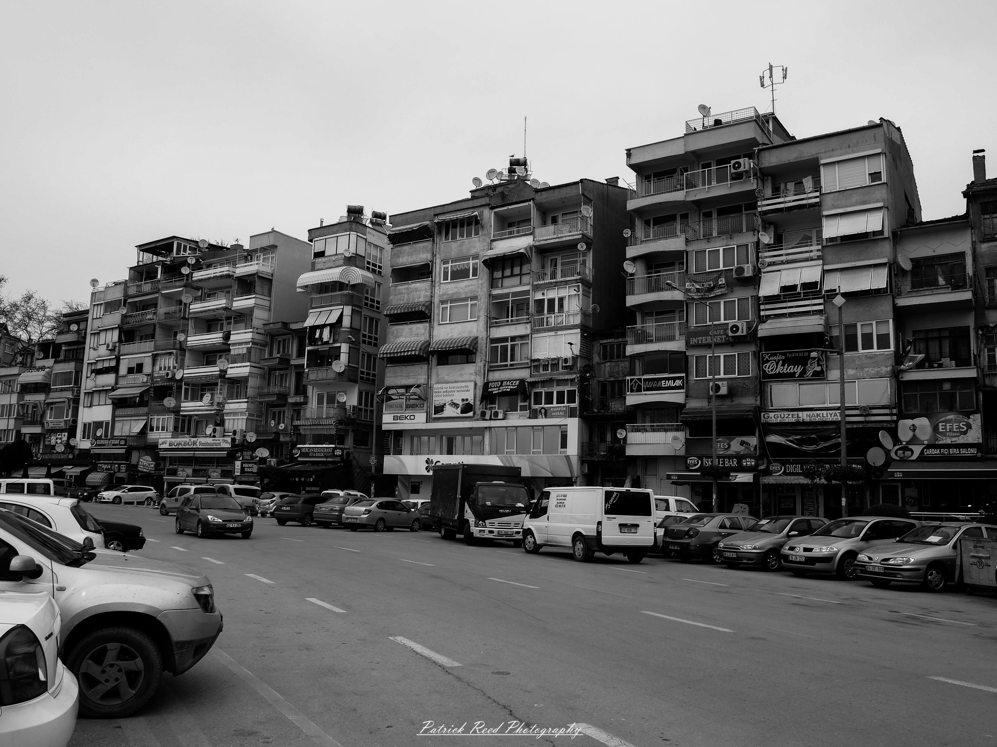 Turkey 4 A series of noir-style street photography scenes set in Istanbul, Turkey, at night. The dimly lit streets and narrow alleys are wet from rain, reflecting the warm glow of streetlights and neon signs. Silhouettes of people walking, some carrying umbrellas, move through the misty atmosphere. The scenes highlight a blend of historical Ottoman architecture, such as arched doorways and intricate stone facades, with modern urban elements like cafes, storefronts, and graffiti. The Bosphorus skyline and glimpses of minarets in the distance add to the cinematic, mysterious ambiance. The overall mood is evocative and steeped in noir storytelling.