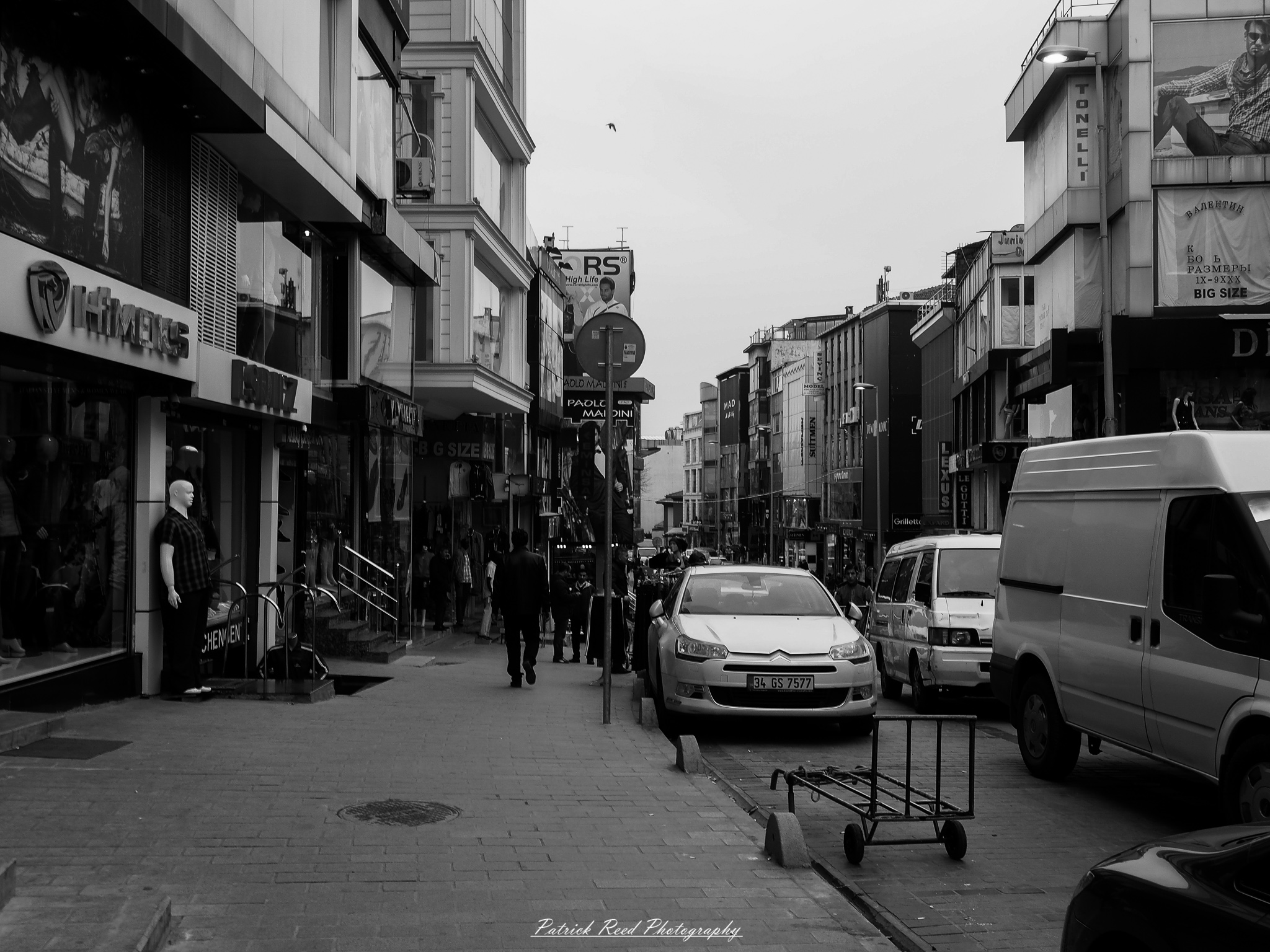 Turkey 9 A series of noir-style street photography scenes set in Istanbul, Turkey, at night. The dimly lit streets and narrow alleys are wet from rain, reflecting the warm glow of streetlights and neon signs. Silhouettes of people walking, some carrying umbrellas, move through the misty atmosphere. The scenes highlight a blend of historical Ottoman architecture, such as arched doorways and intricate stone facades, with modern urban elements like cafes, storefronts, and graffiti. The Bosphorus skyline and glimpses of minarets in the distance add to the cinematic, mysterious ambiance. The overall mood is evocative and steeped in noir storytelling.