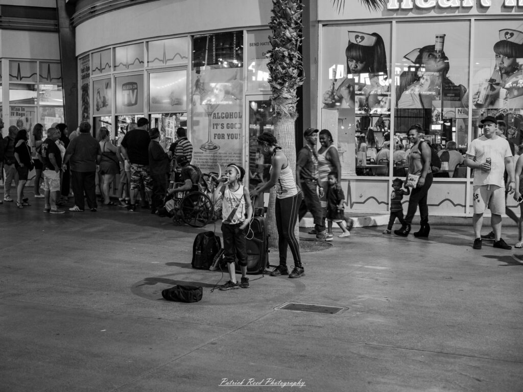 A series of noir-style street photography scenes set in Las Vegas, Nevada, at night. The rain-slicked streets reflect the vibrant glow of neon signs from casinos, motels, and diners. Silhouettes of people walking under umbrellas or leaning against lampposts add a sense of mystery and intrigue. The scenes capture a mix of classic Vegas landmarks, vintage signage, and gritty back alleys with graffiti and scattered debris. The dramatic lighting emphasizes shadows and contrasts, creating a moody, cinematic ambiance that evokes the essence of noir storytelling in a bustling yet shadowy cityscape.