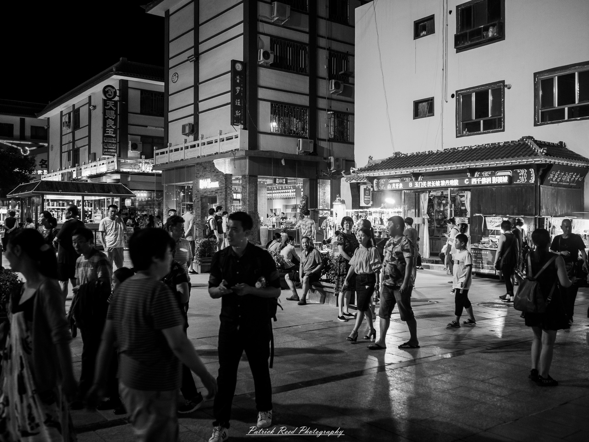A series of noir-style street photography scenes set in Dunhuang, China, at night. The dimly lit streets and narrow alleyways reflect the soft glow of lanterns and neon signs from small shops and market stalls. Silhouettes of people walk through the misty night, some in traditional robes, adding a sense of mystery. The historic Silk Road atmosphere is highlighted by earthen architecture, intricate wooden doors, and desert dust settling on the pavement. Modern elements like motorbikes and distant headlights contrast with the ancient setting. The deep shadows and warm, flickering lights create a cinematic, moody ambiance, blending noir aesthetics with Dunhuang’s rich cultural history.