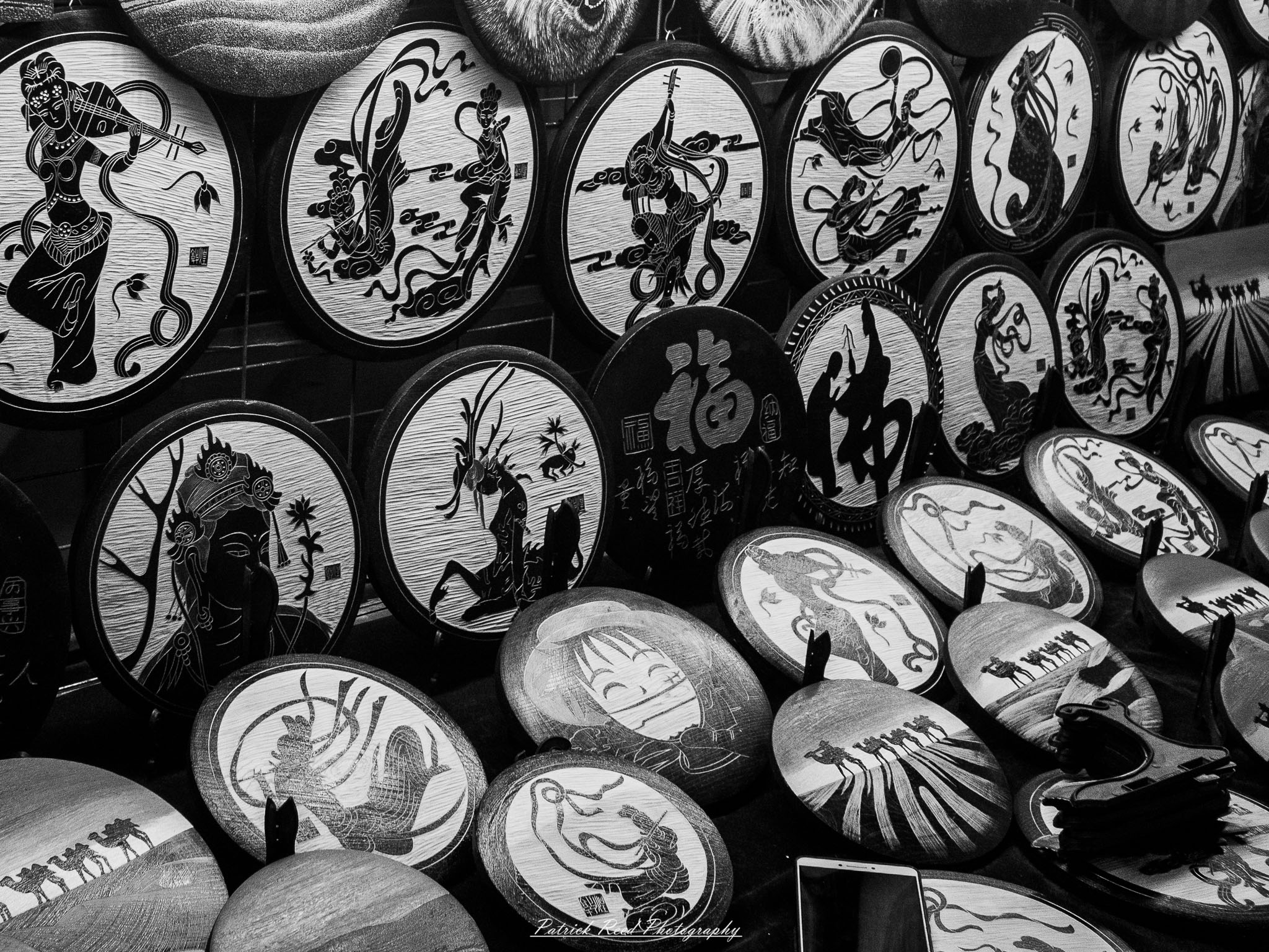 A series of noir-style street photography scenes set in Dunhuang, China, at night. The dimly lit streets and narrow alleyways reflect the soft glow of lanterns and neon signs from small shops and market stalls. Silhouettes of people walk through the misty night, some in traditional robes, adding a sense of mystery. The historic Silk Road atmosphere is highlighted by earthen architecture, intricate wooden doors, and desert dust settling on the pavement. Modern elements like motorbikes and distant headlights contrast with the ancient setting. The deep shadows and warm, flickering lights create a cinematic, moody ambiance, blending noir aesthetics with Dunhuang’s rich cultural history.