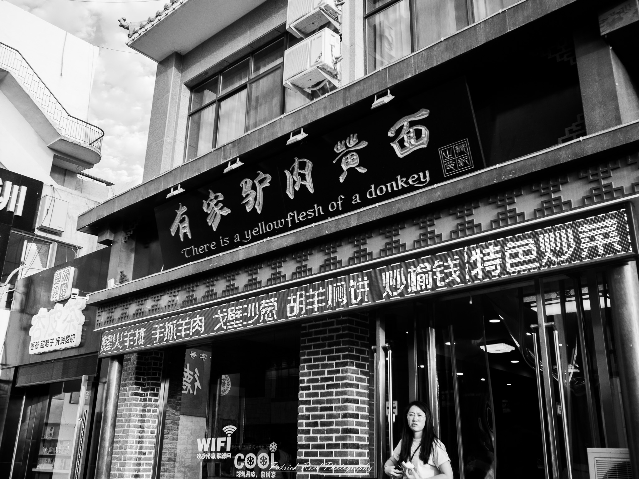 A series of noir-style street photography scenes set in Dunhuang, China, at night. The dimly lit streets and narrow alleyways reflect the soft glow of lanterns and neon signs from small shops and market stalls. Silhouettes of people walk through the misty night, some in traditional robes, adding a sense of mystery. The historic Silk Road atmosphere is highlighted by earthen architecture, intricate wooden doors, and desert dust settling on the pavement. Modern elements like motorbikes and distant headlights contrast with the ancient setting. The deep shadows and warm, flickering lights create a cinematic, moody ambiance, blending noir aesthetics with Dunhuang’s rich cultural history.