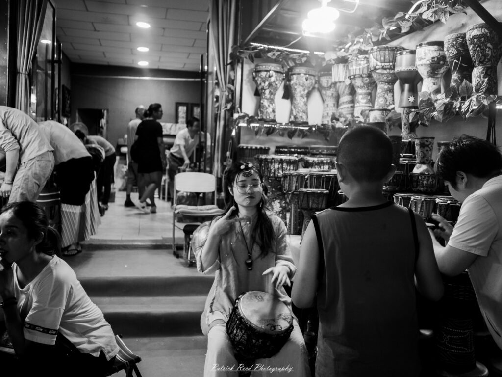A series of noir-style street photography scenes set in Dunhuang, China, at night. The dimly lit streets and narrow alleyways reflect the soft glow of lanterns and neon signs from small shops and market stalls. Silhouettes of people walk through the misty night, some in traditional robes, adding a sense of mystery. The historic Silk Road atmosphere is highlighted by earthen architecture, intricate wooden doors, and desert dust settling on the pavement. Modern elements like motorbikes and distant headlights contrast with the ancient setting. The deep shadows and warm, flickering lights create a cinematic, moody ambiance, blending noir aesthetics with Dunhuang’s rich cultural history.