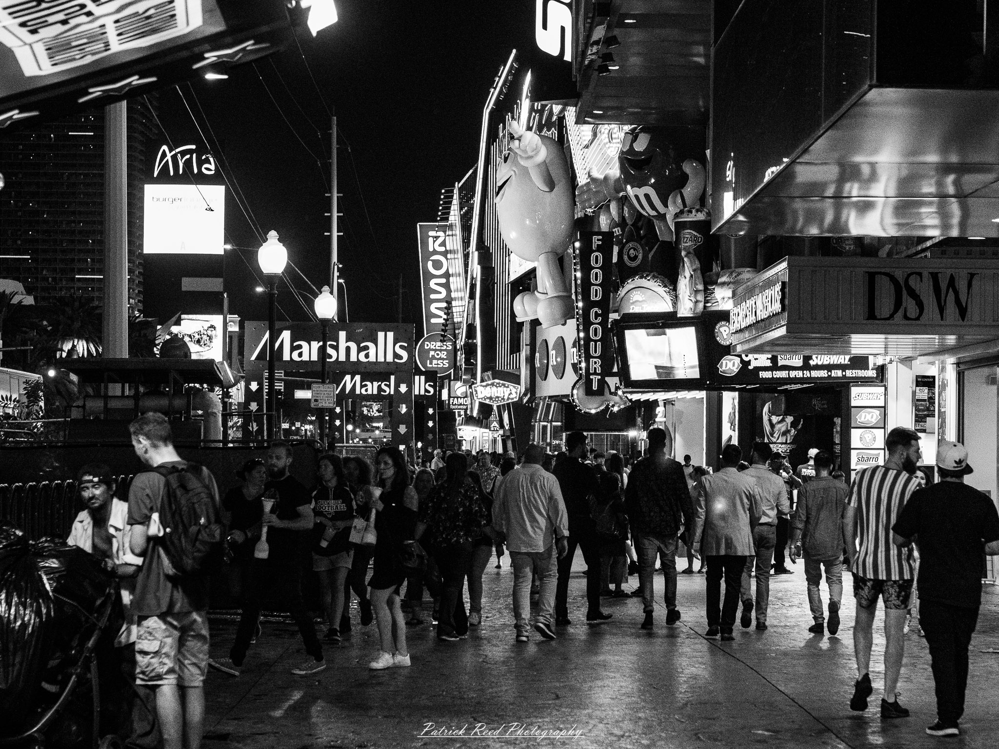 Vegas 37 A series of noir-style street photography scenes set in Las Vegas, Nevada, at night. The rain-slicked streets reflect the vibrant glow of neon signs from casinos, motels, and diners. Silhouettes of people walking under umbrellas or leaning against lampposts add a sense of mystery and intrigue. The scenes capture a mix of classic Vegas landmarks, vintage signage, and gritty back alleys with graffiti and scattered debris. The dramatic lighting emphasizes shadows and contrasts, creating a moody, cinematic ambiance that evokes the essence of noir storytelling in a bustling yet shadowy cityscape.