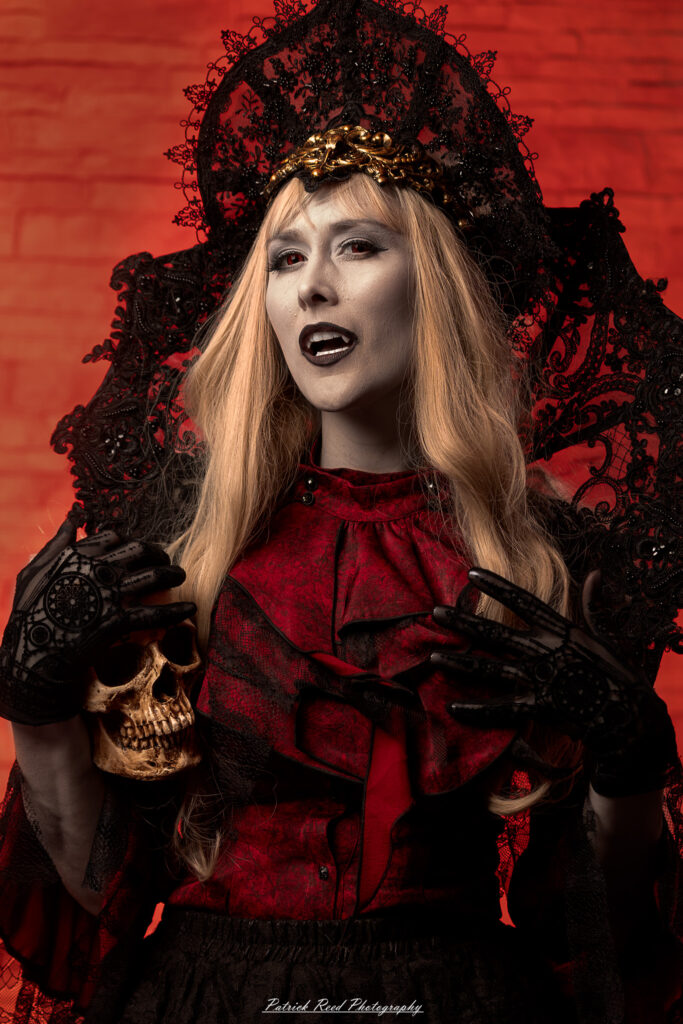 Alt text: Portrait of a woman in vampire cosplay named Lady Thorn, photographed on June 28, 2025. She is posed against a vivid red background, styled with gothic elements and dramatic expression.