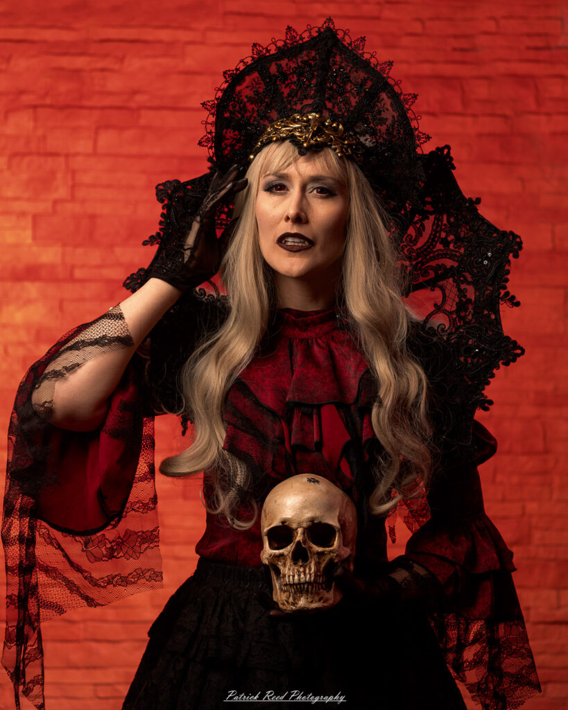 Alt text: Portrait of a woman in vampire cosplay named Lady Thorn, photographed on June 28, 2025. She is posed against a vivid red background, styled with gothic elements and dramatic expression.